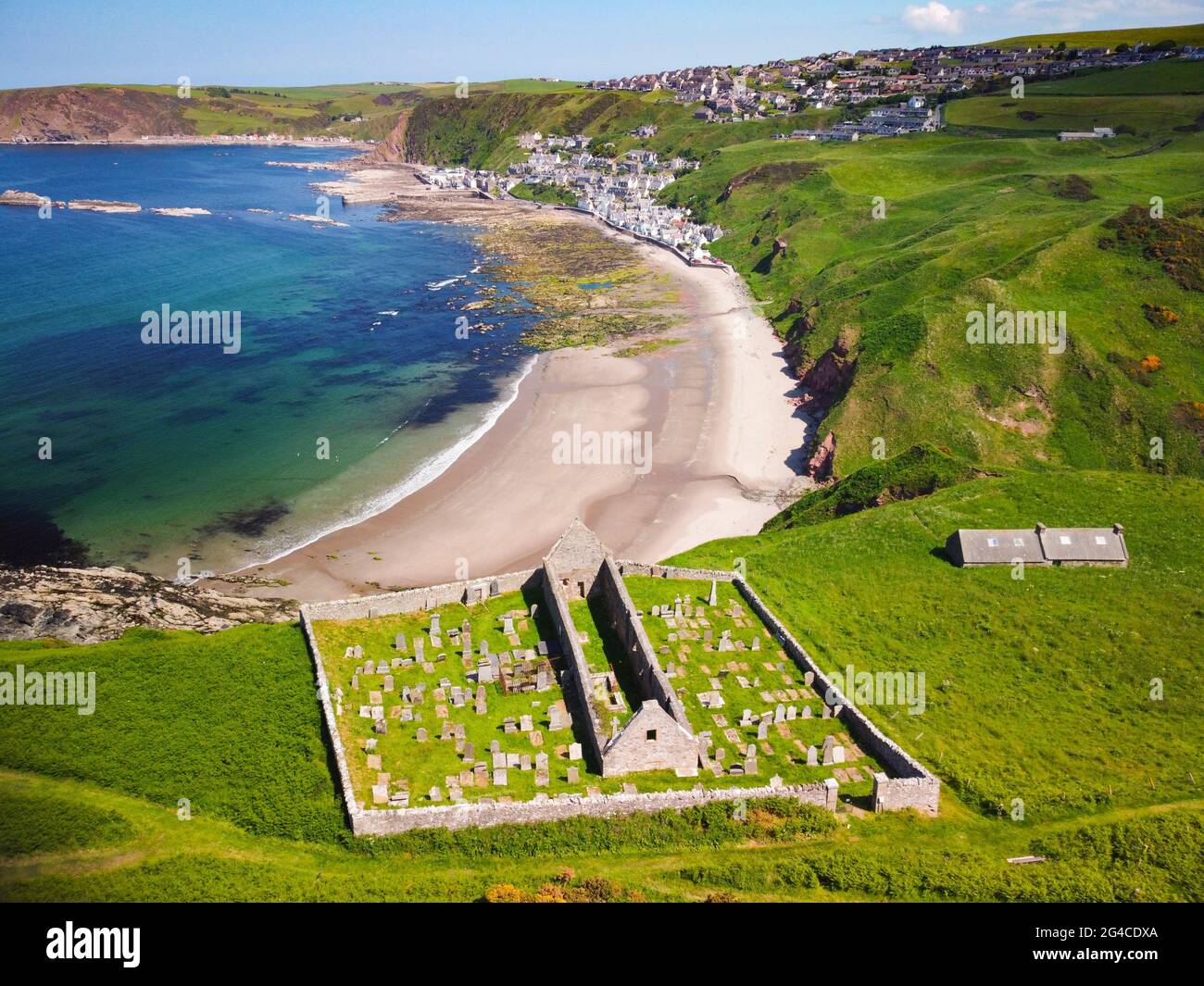 Vista aerea dal drone della chiesa di San Giovanni e Kirkyard che domina il villaggio di Gardenstown sulla costa di Moray firth ad Aberdeenshire, Scozia, Regno Unito Foto Stock