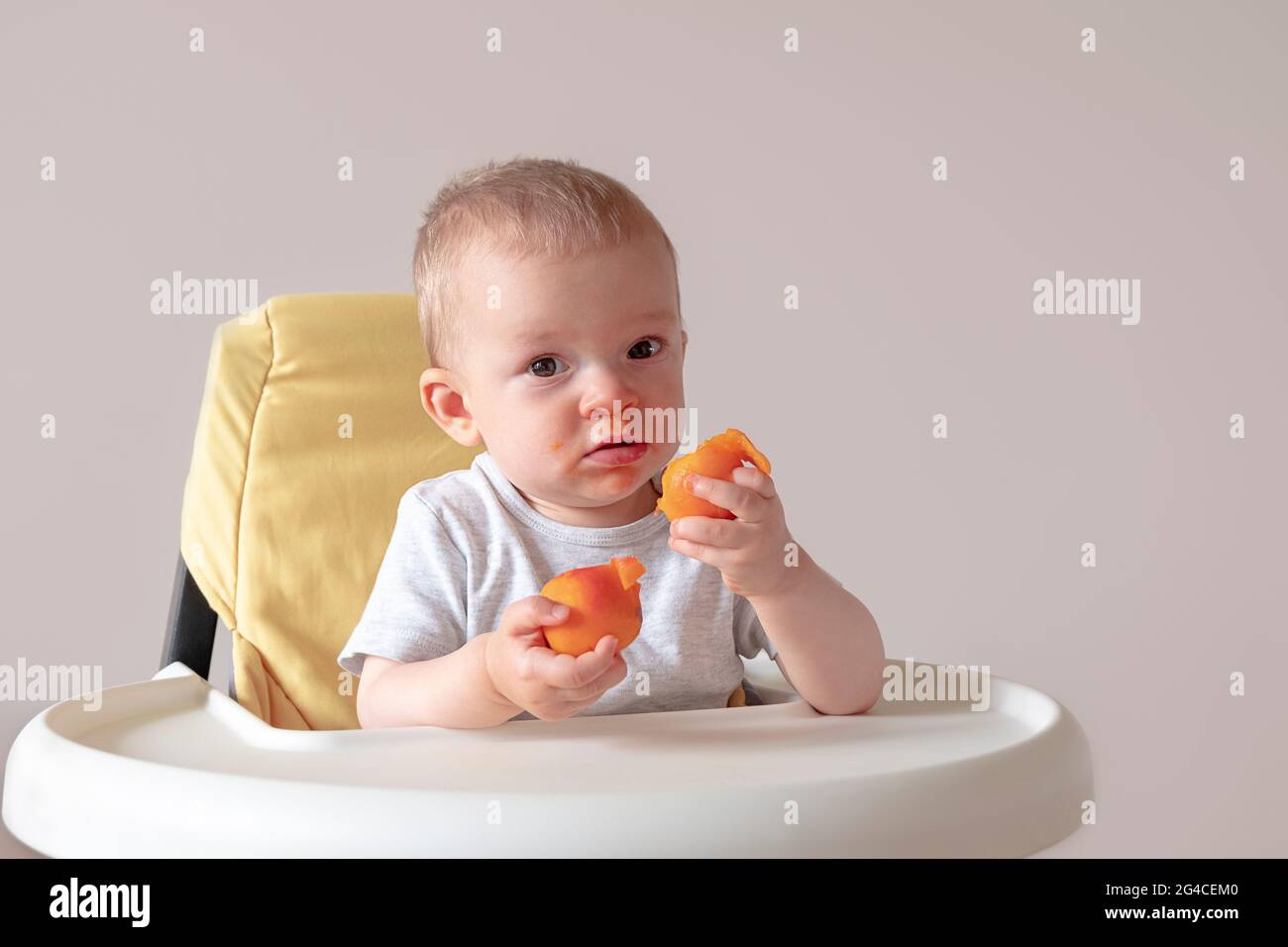 Alimenti per bambini, concetto di nutrizione. Bambino seduto ad un tavolo con le albicocche in mano Foto Stock