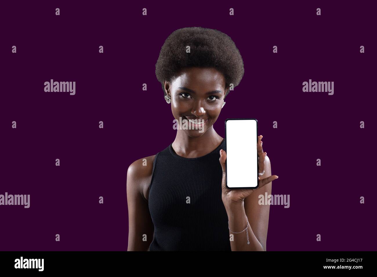 Donna nera afroamericana sorridente che punta con il dito su modello vuoto telefono cellulare schermo bianco su sfondo Lilac Foto Stock