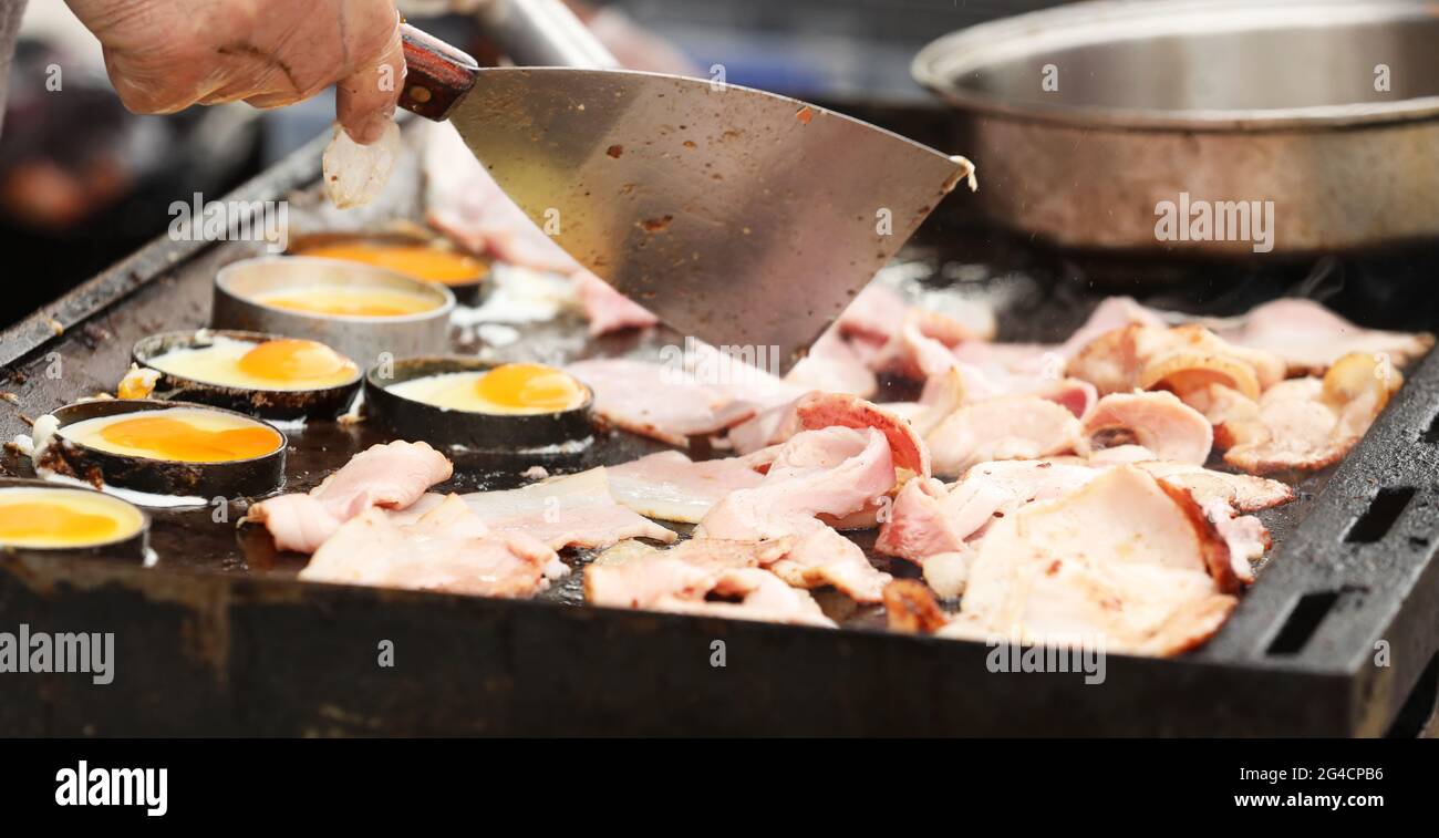 Cucinare un gran numero di pancetta e uova su una griglia barbecue o piatto caldo. Foto Stock