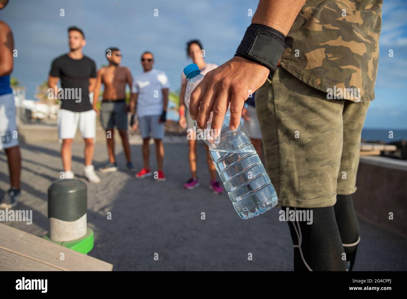 Primo piano sulla bottiglia d'acqua tenuta da un uomo durante un allenamento all'aperto con un gruppo di atleti. L'importanza dell'acqua. Concetto di idratazione durante s. Foto Stock