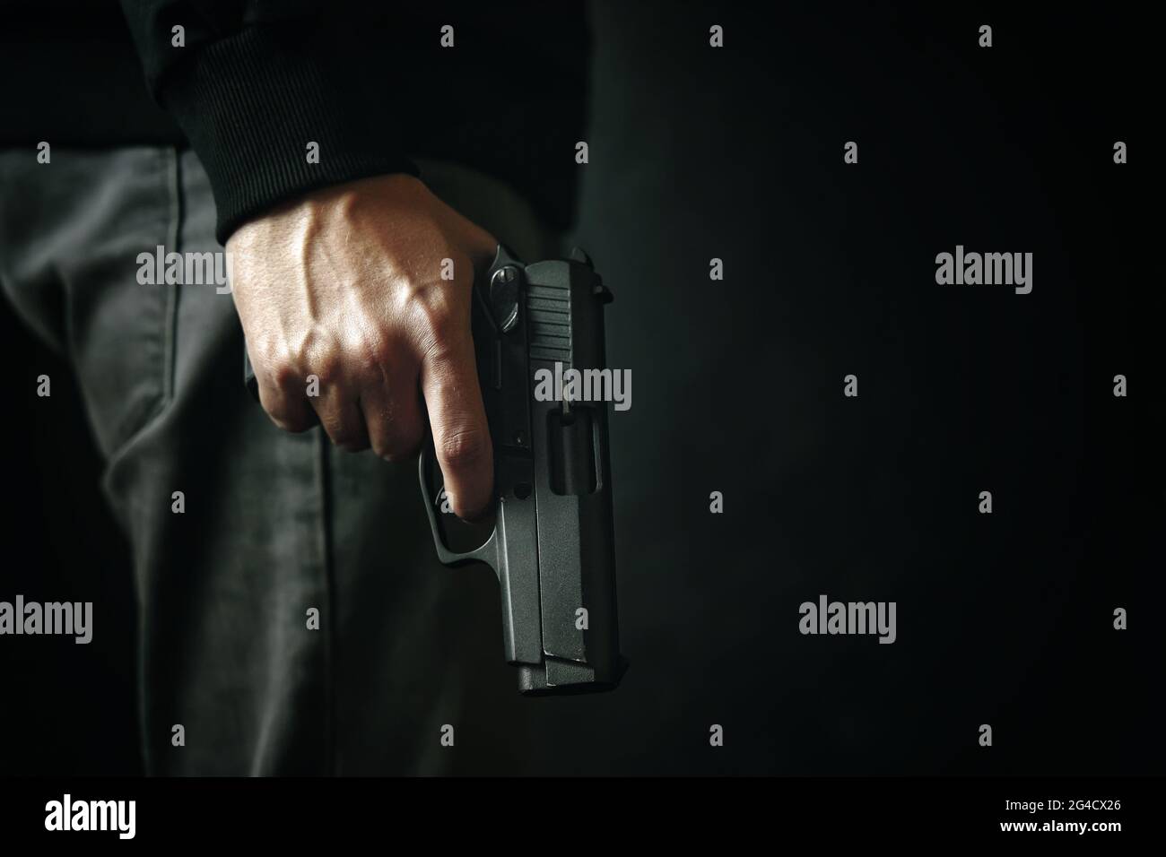 Criminale con rivoltatore su sfondo scuro. Arma da fuoco in mano dell'uomo. Difesa o attacco. Assassino o ladro armato. Pistola con tamburo. Foto Stock