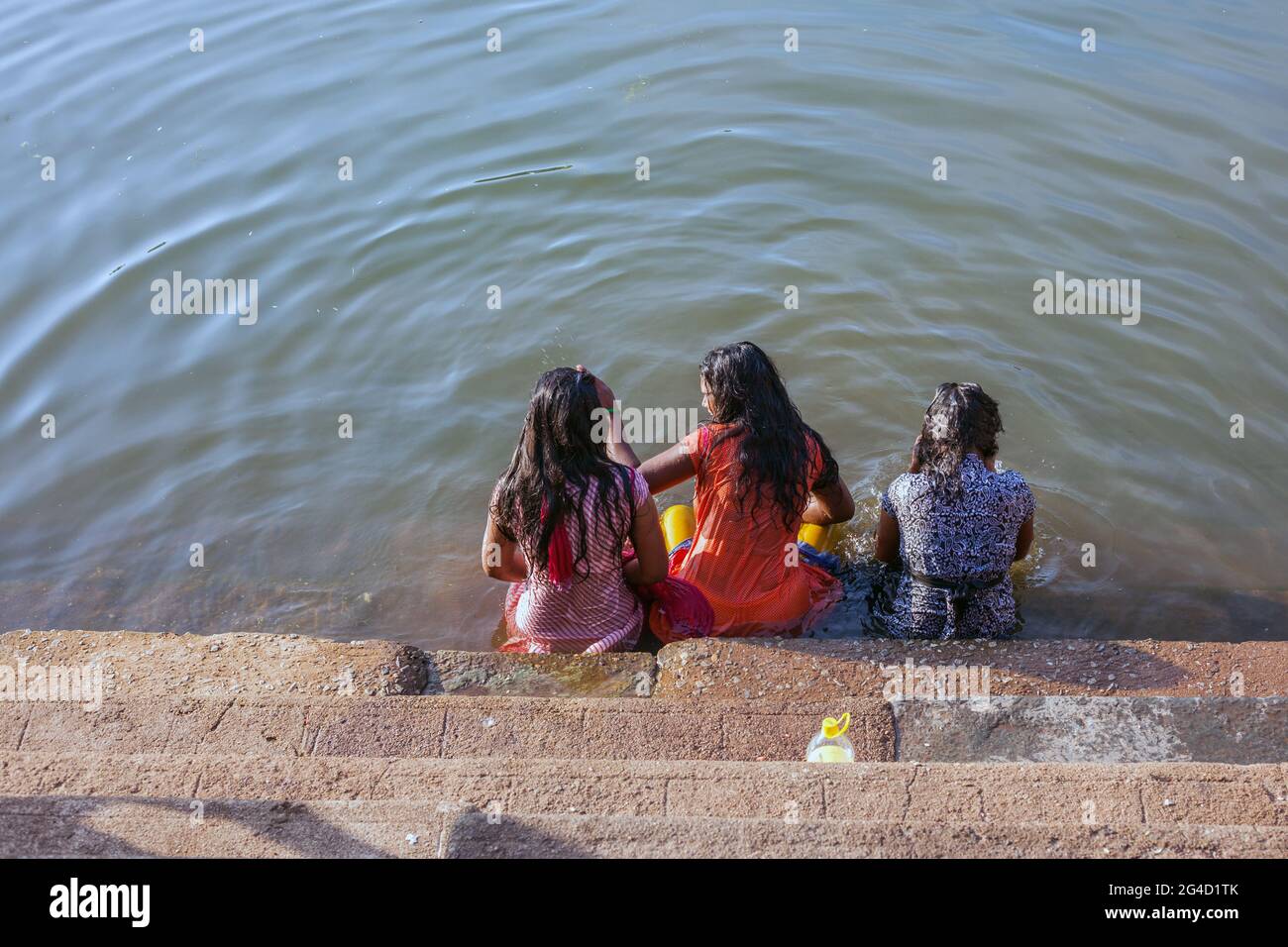 Tre femmine si siedono sui gradini parzialmente sommersi nell'acqua al serbatoio d'acqua di Koti Tirrtha, Gokarna, Karnataka, India Foto Stock