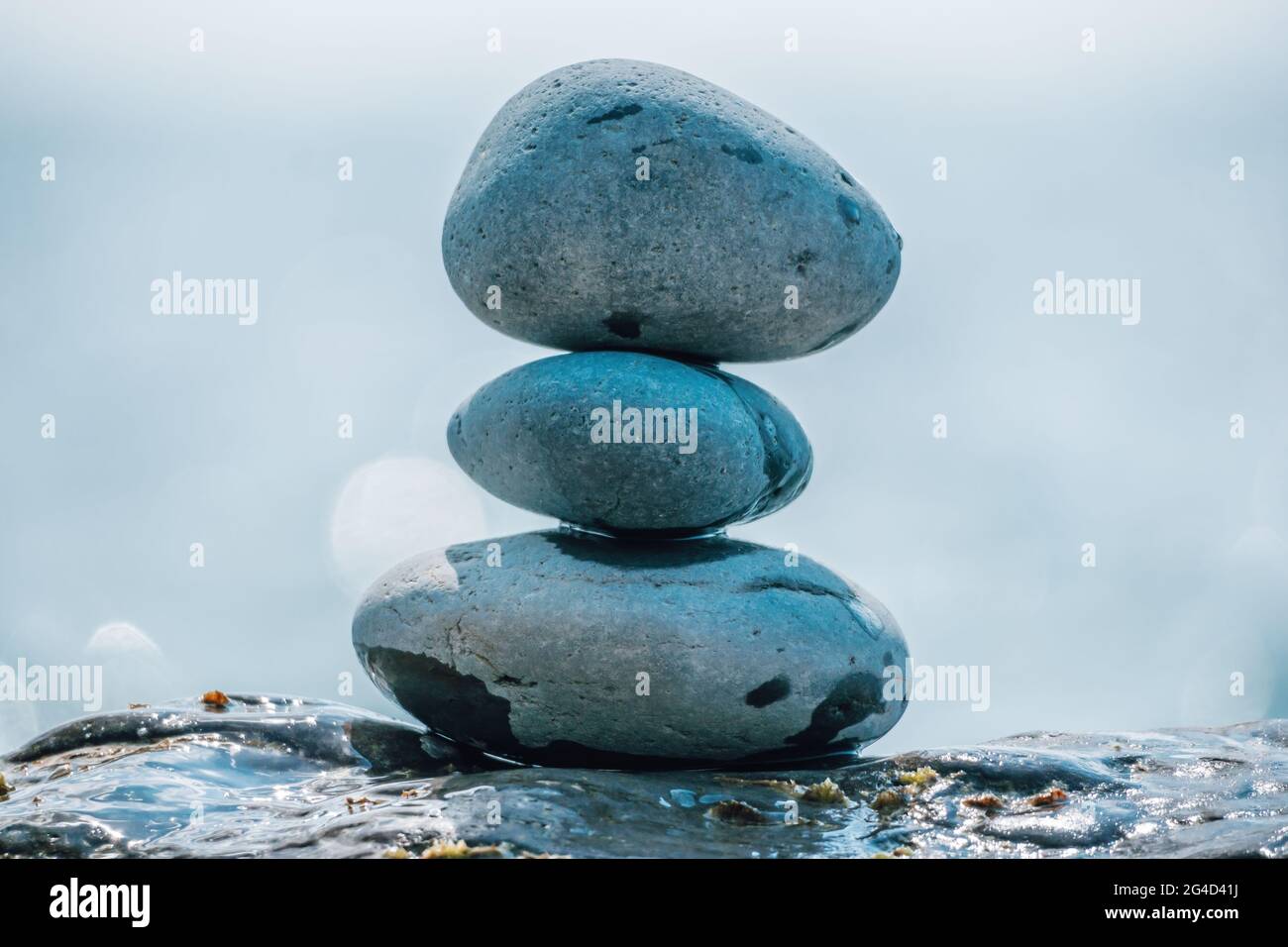 Equilibrata piramide di ciottoli sulla spiaggia in una giornata di sole. Abstract Sea bokeh sullo sfondo. Messa a fuoco selettiva. Pietre Zen sulla spiaggia di mare, meditazione Foto Stock