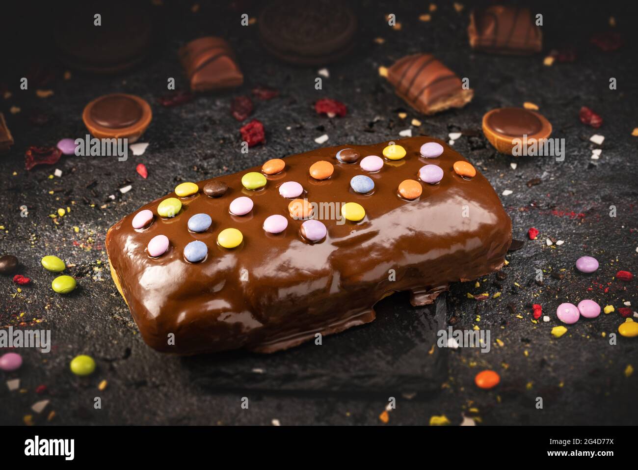 Concetto di cibo dolce veloce, ciambella quadrangolare smaltata al cioccolato dolce decorata con caramelle firecracker Foto Stock