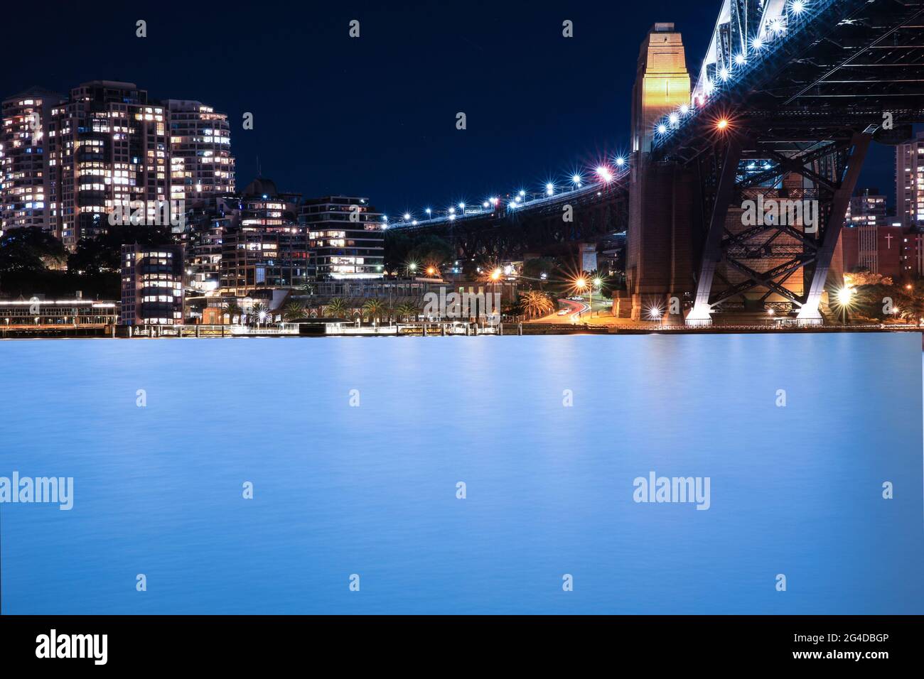 Vista panoramica notturna del porto di Sydney e dello skyline della città di Circular Quay il ponte NSW Australia. Luci luminose che riflettono l'acqua Pink Moon Foto Stock