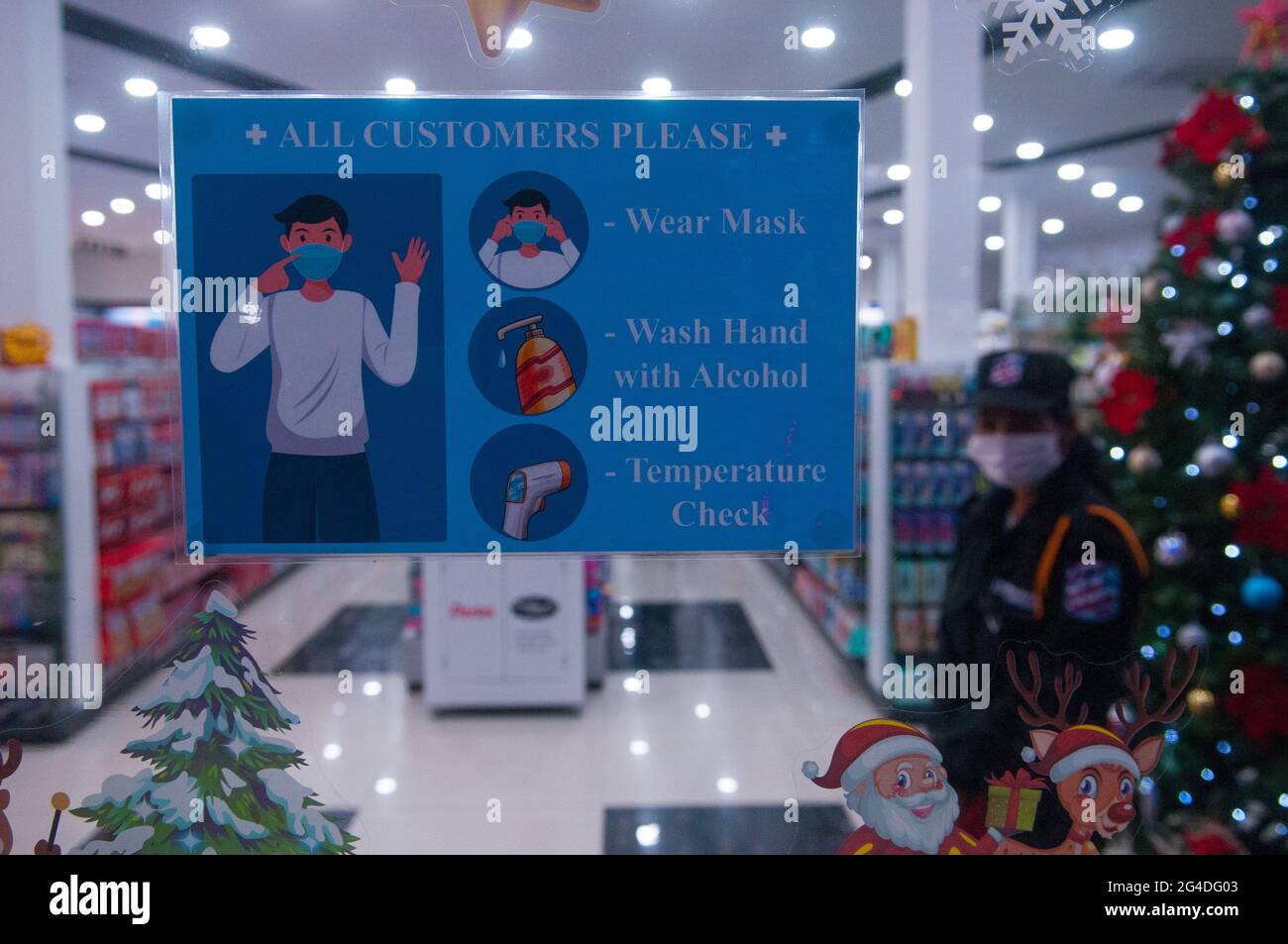 COVID - 19 cartello di avvertimento all'ingresso di un negozio vuoto che vende alberi di Natale e decorazioni con una guardia di sicurezza femminile che indossa una maschera protettiva / copertura durante la pandemia del coronavirus. Steung Meanchey, Phnom Penh, Cambogia. 1° dicembre 2020. © Kraig Lieb Foto Stock