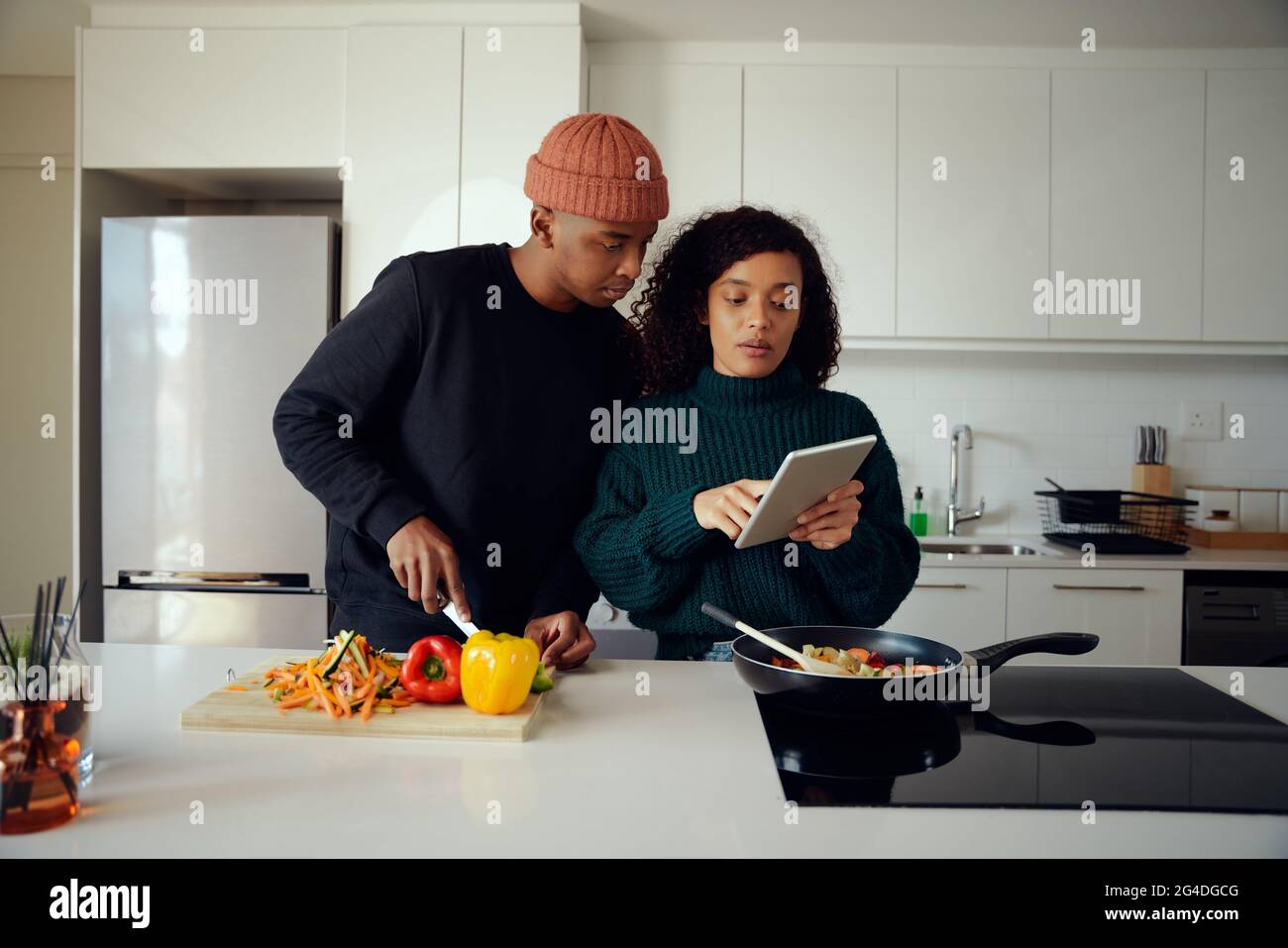 Giovane gara mista coppia cucina cibo in cucina e utilizzando un tablet. Coppia che guarda il tablet per la ricetta del cibo. Foto di alta qualità Foto Stock