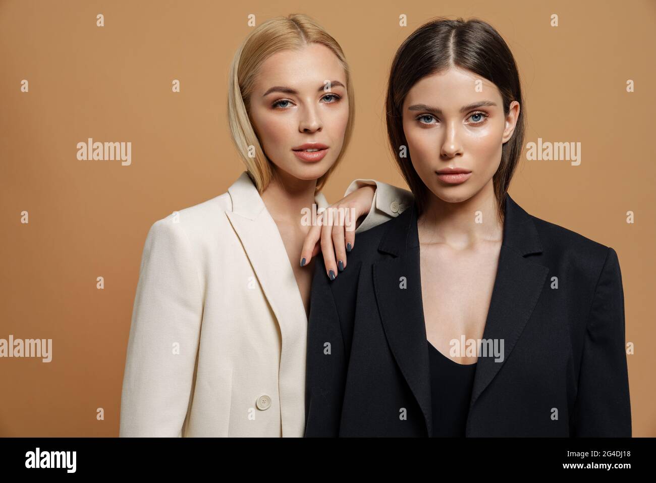 Due belle donne eleganti che indossano giacche intelligenti che si posano  insieme isolati su sfondo beige Foto stock - Alamy