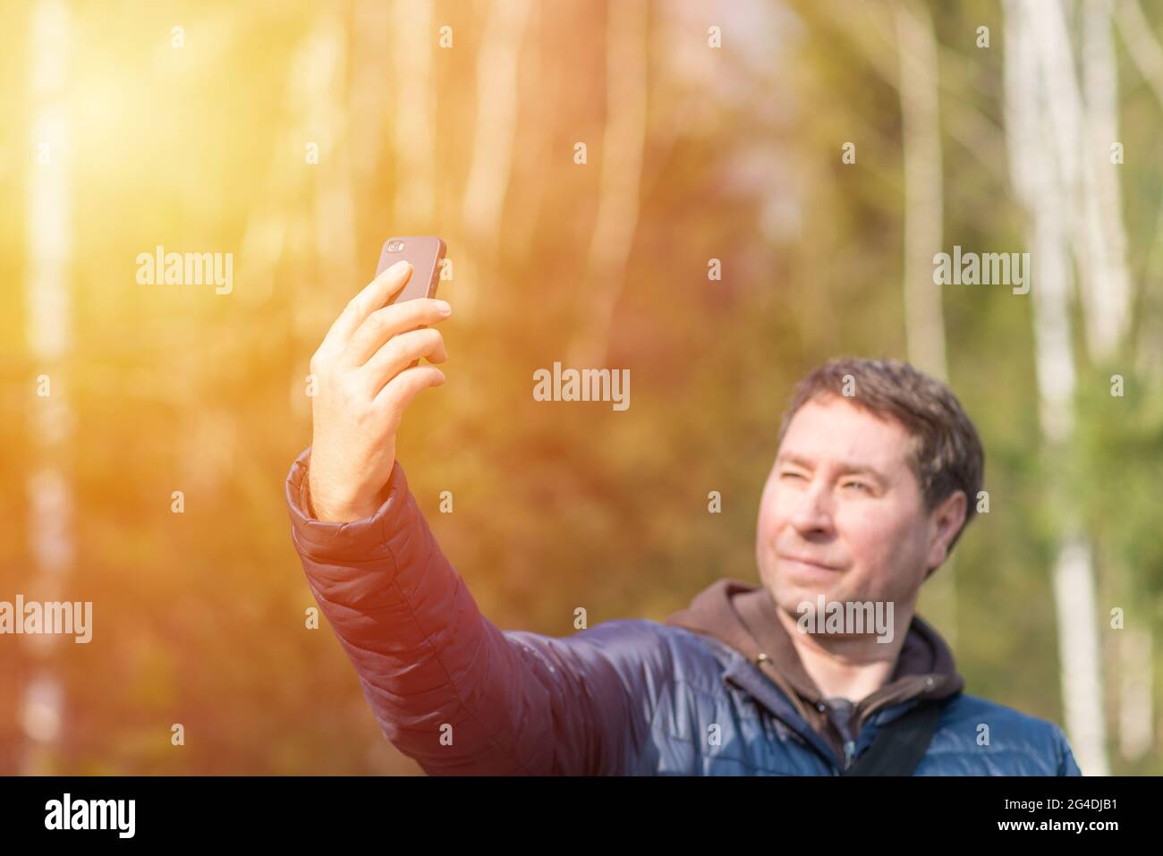 Un uomo di 40 anni con il suo smartphone cellulare alla ricerca del segnale di ricezione nella foresta primaverile soleggiata. Foto Stock