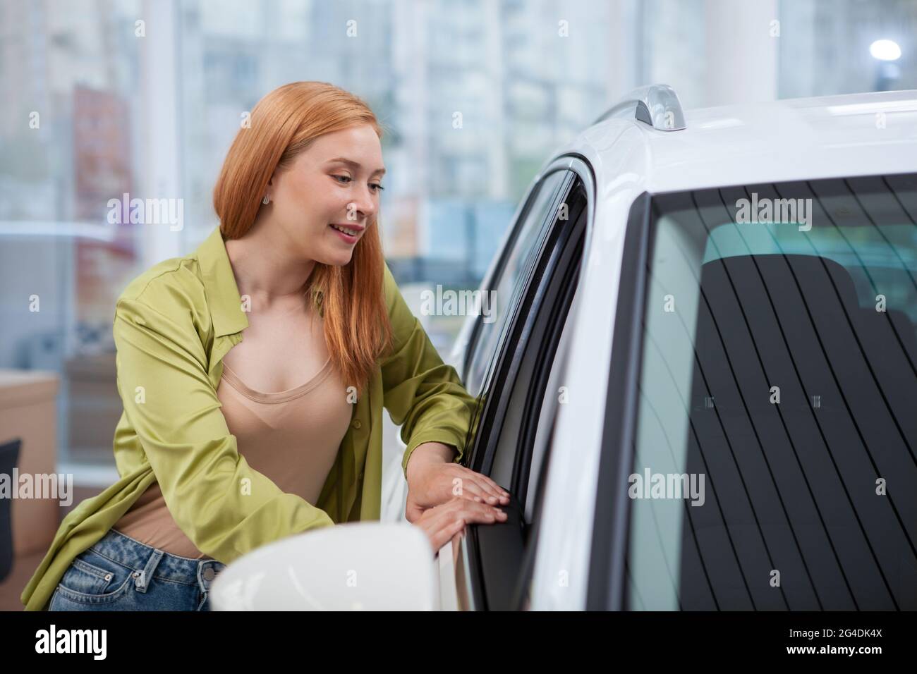 Giovane donna sorridente, guardando dentro l'automobile per la vendita alla concessionaria di automobile Foto Stock