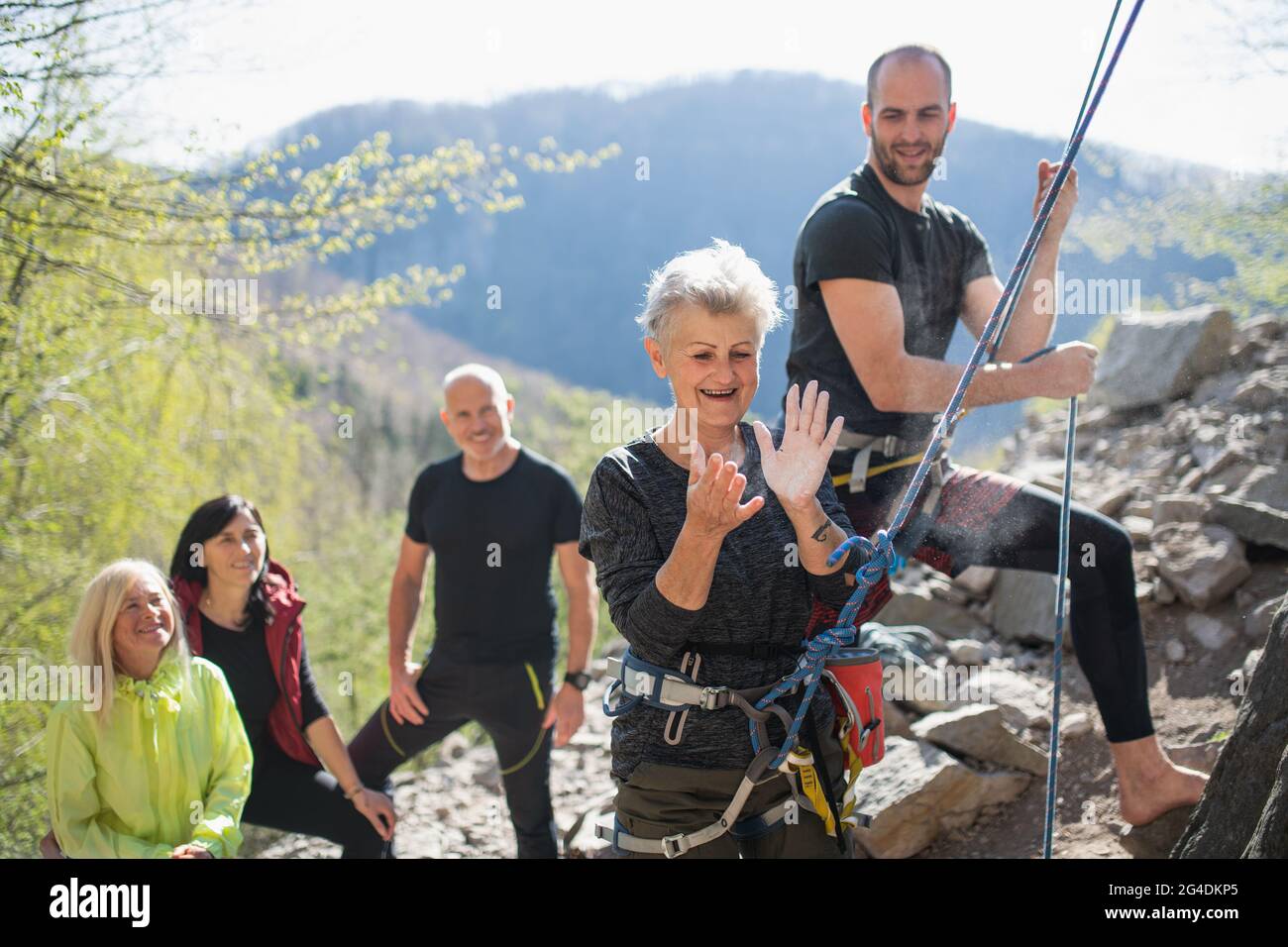 Gruppo di anziani con istruttore utilizzando gesso prima di arrampicare rocce all'aperto in natura, stile di vita attivo. Foto Stock