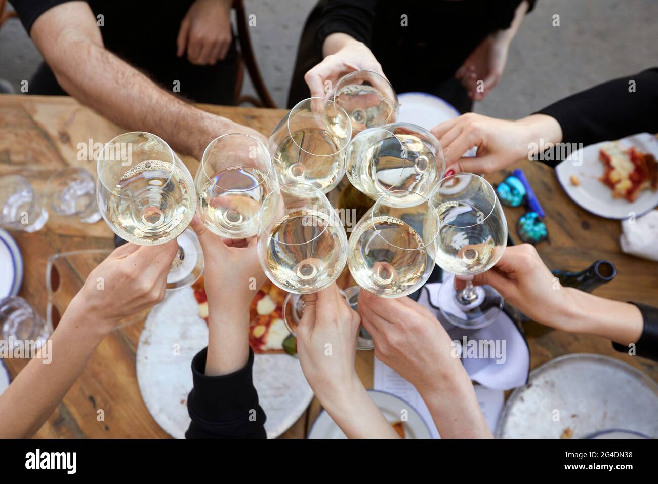 Dall'alto del gruppo di persone anonime raccolto che si riuniscono intorno al tavolo con pizza e bicchieri da clinking con vino bianco durante la festa Foto Stock
