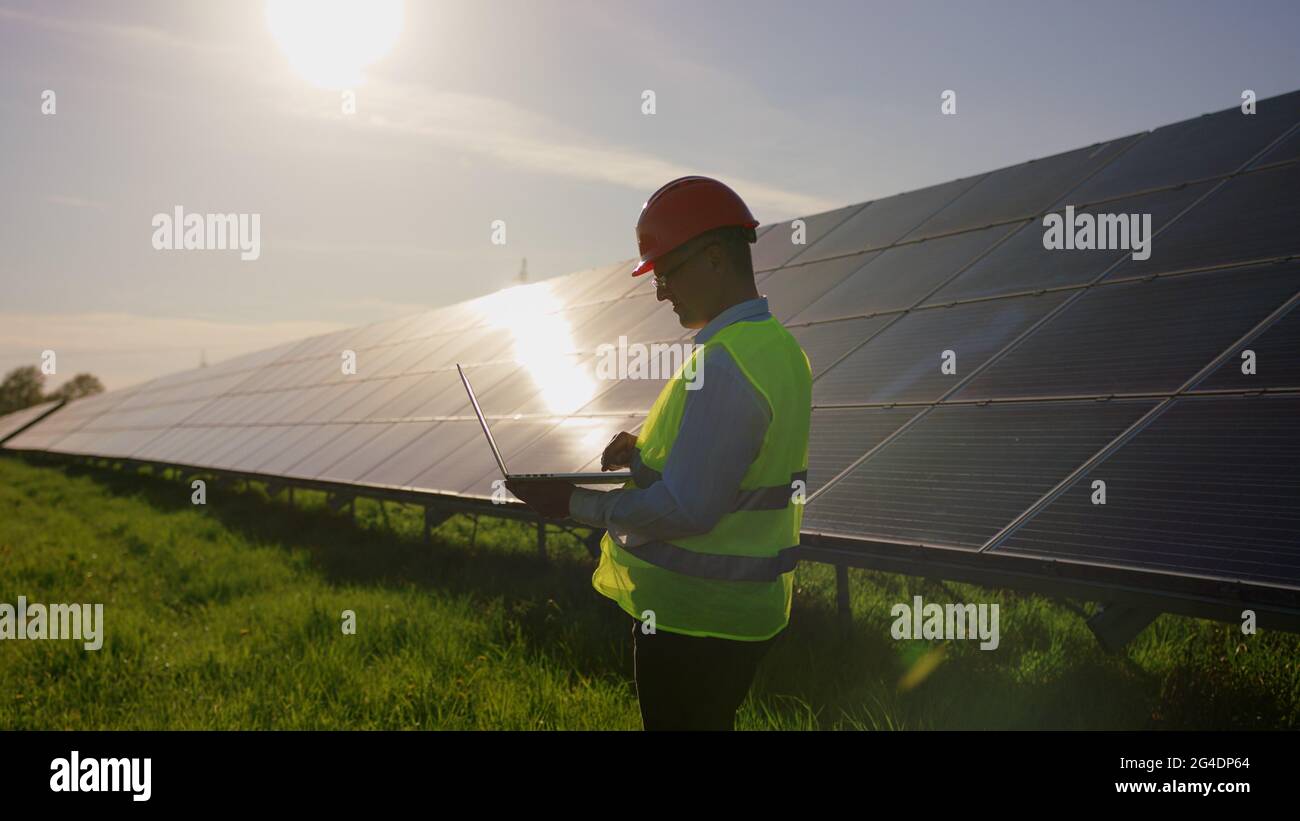 Ingegnere lavoro uso portatile stand vicino a batterie solari costruzione energia rinnovabile lavoratore uomo tecnologia moderna energia elettrica movimento lento Foto Stock