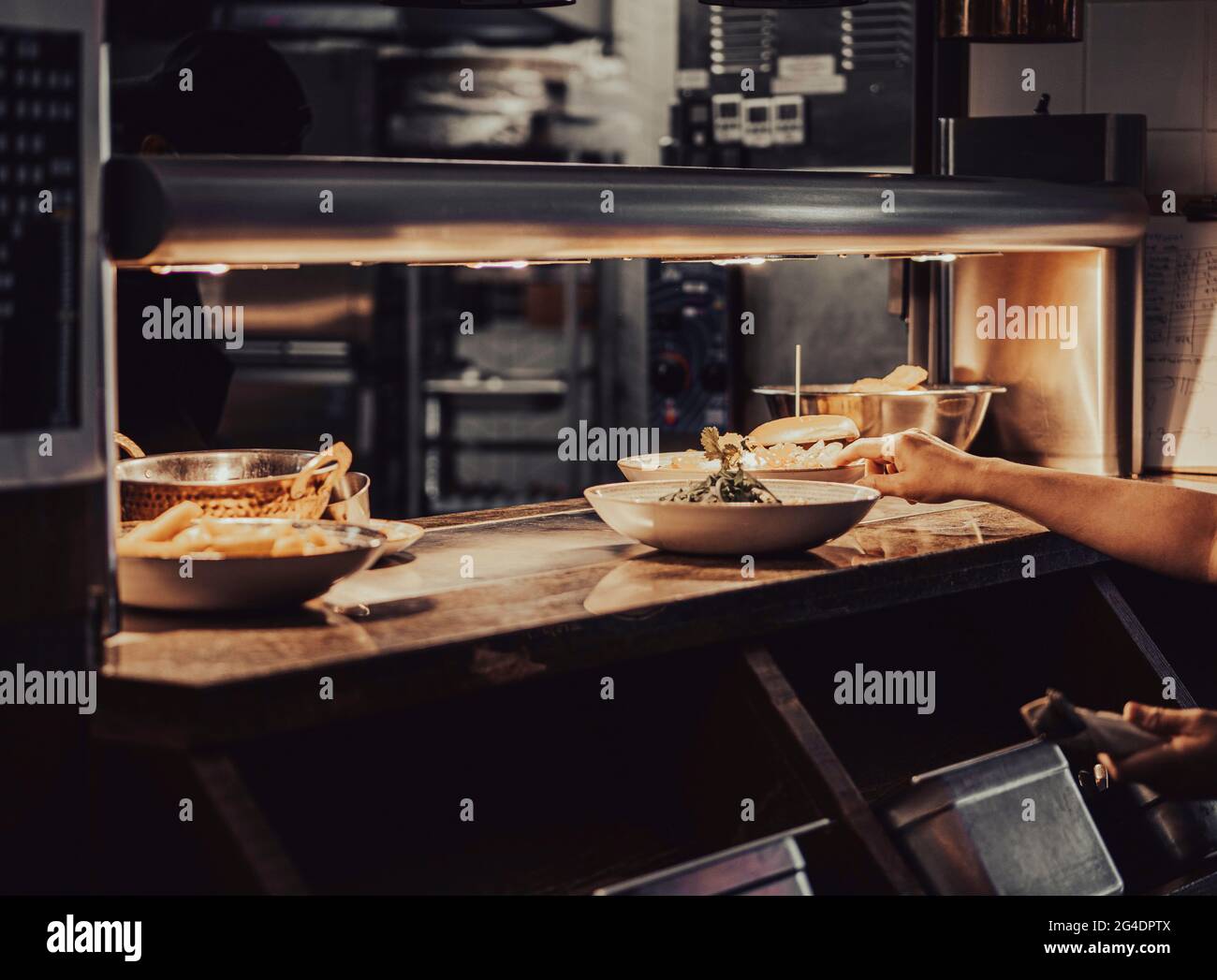 Un cameriere del cibo preleva un piatto da un bancone di servizio del cibo. I piatti e le ciotole sotto la luce sono in attesa Foto Stock