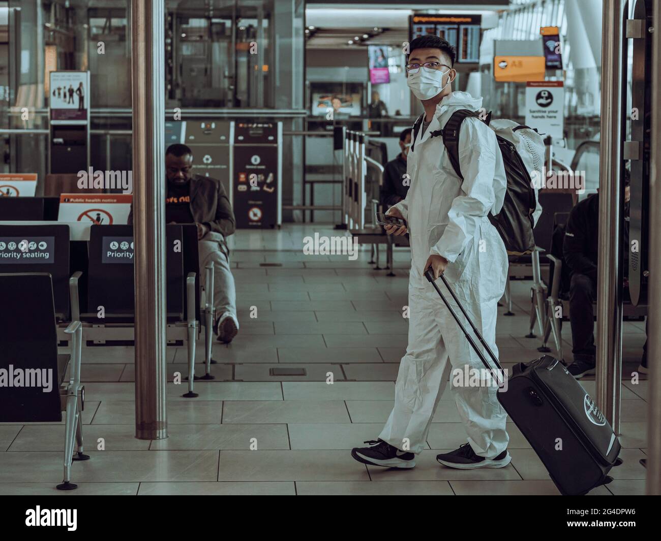 Un viaggiatore in completo DPI cammina in un terminal dell'aeroporto. Il passeggero vestito con una tuta di protezione completa attraversa il terminal passeggeri Foto Stock
