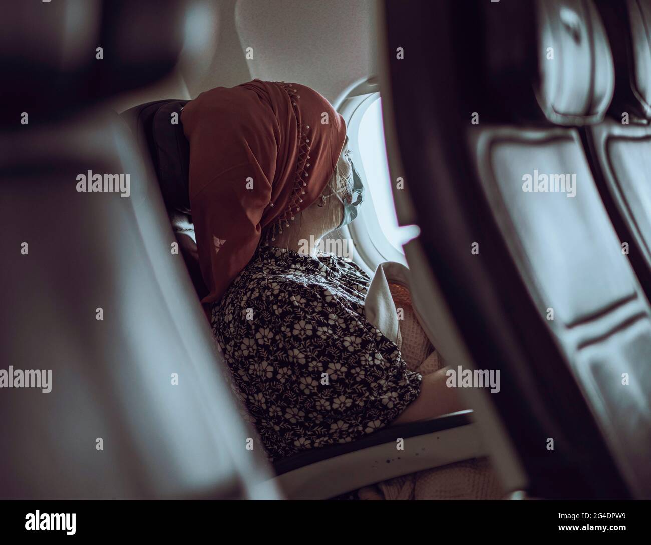 Una donna che dormiva viaggiatore si siede a una finestra di aeroplano. La donna che indossa la maschera si siede in una finestra soleggiata che dorme e guarda la vista fuori dalla finestra Foto Stock