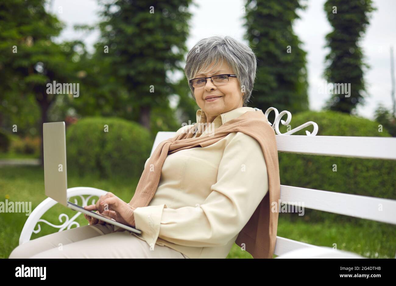 Ritratto di una donna anziana felice seduta su una panchina del parco e utilizzando il suo computer portatile Foto Stock