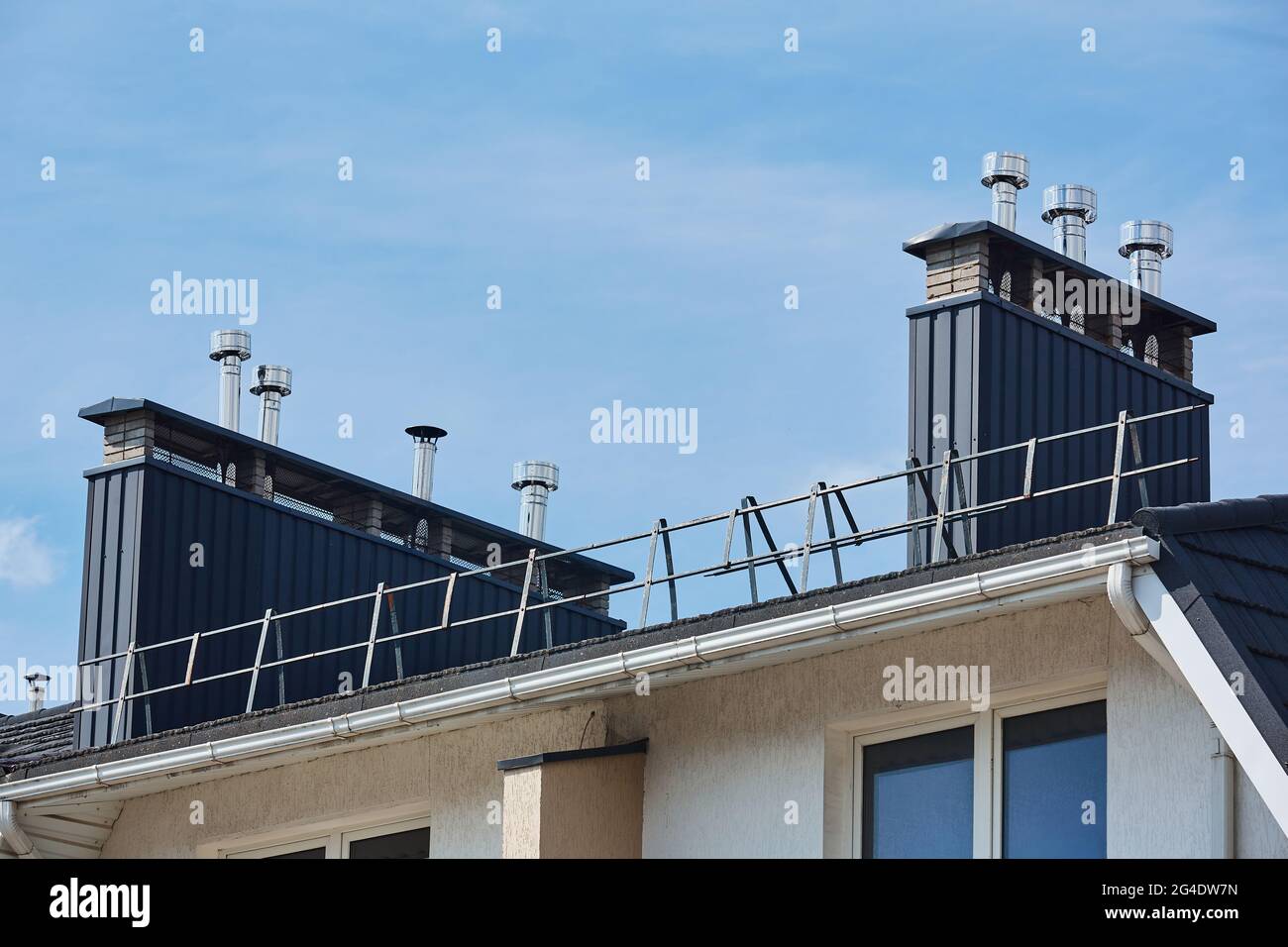 Vista ravvicinata del tubo in pietra di mattoni coperto di lamiere e una scatola nera di fumo sul tetto. Tubo di ventilazione sul tetto della casa moderna Foto Stock