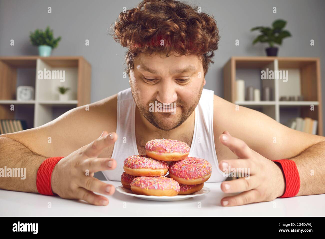 Divertente uomo chubby guardando piatto di dolci tentanti ciambelle con amore e adorazione Foto Stock