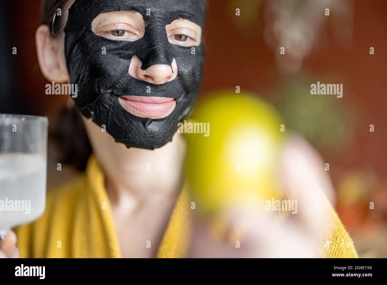 Ritratto di una giovane donna in maschera di pulizia nera sul viso con un bicchiere d'acqua Foto Stock