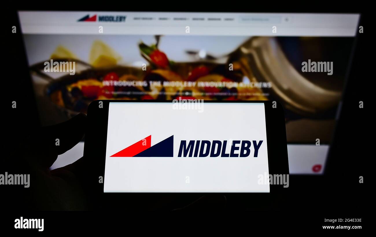 Persona che tiene il cellulare con il logo della società americana di attrezzature da cucina Middleby Corporation sullo schermo di fronte alla pagina web. Mettere a fuoco il display del telefono. Foto Stock