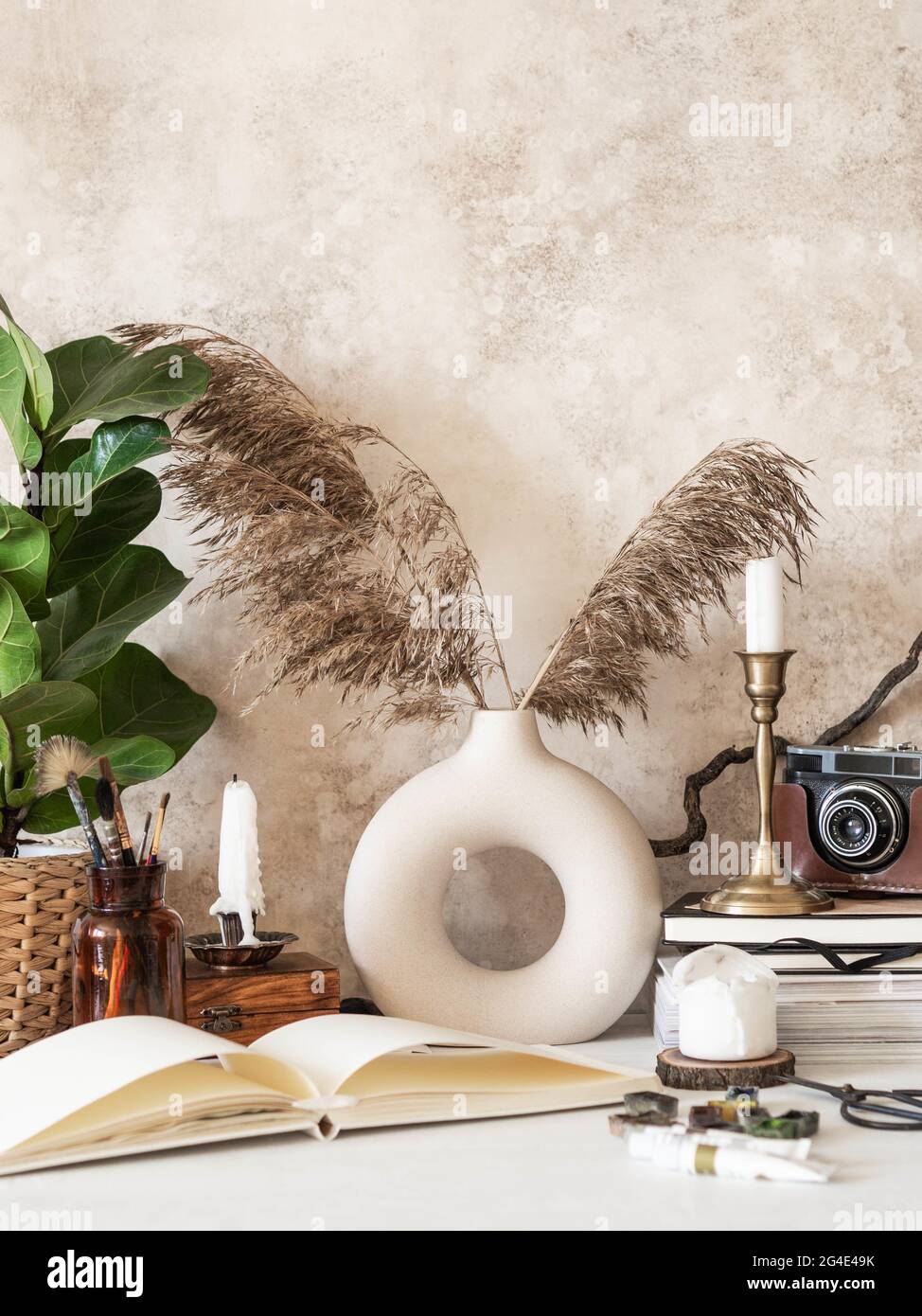 Scrivania dell'artista con vari oggetti retrò, pianta della casa in vaso, vaso con canne secche e drawing pad aperto e vernici pronte al lavoro Foto Stock