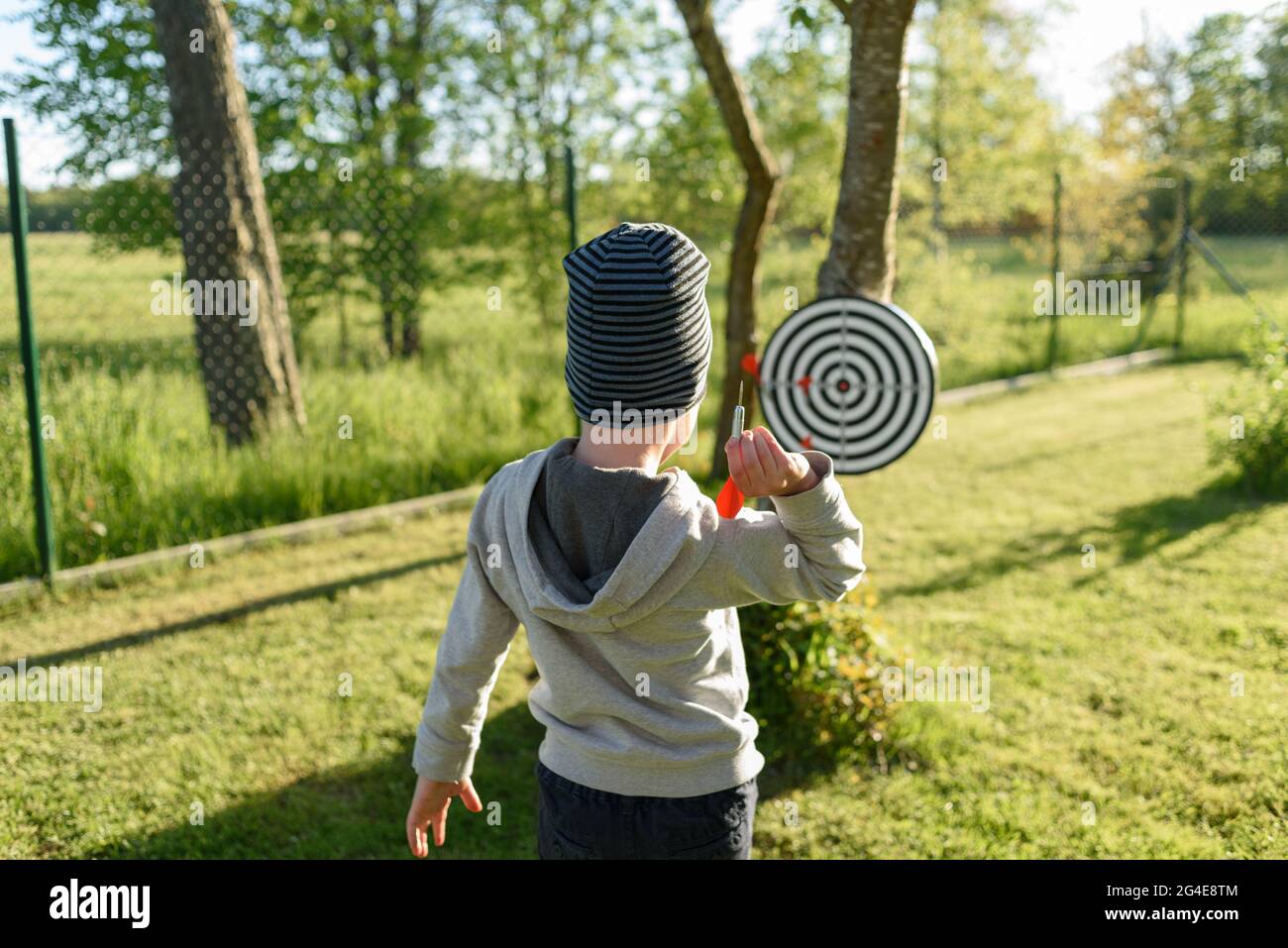 Ragazzo che gioca freccette in cortile, trottando frecce per bersaglio Foto Stock