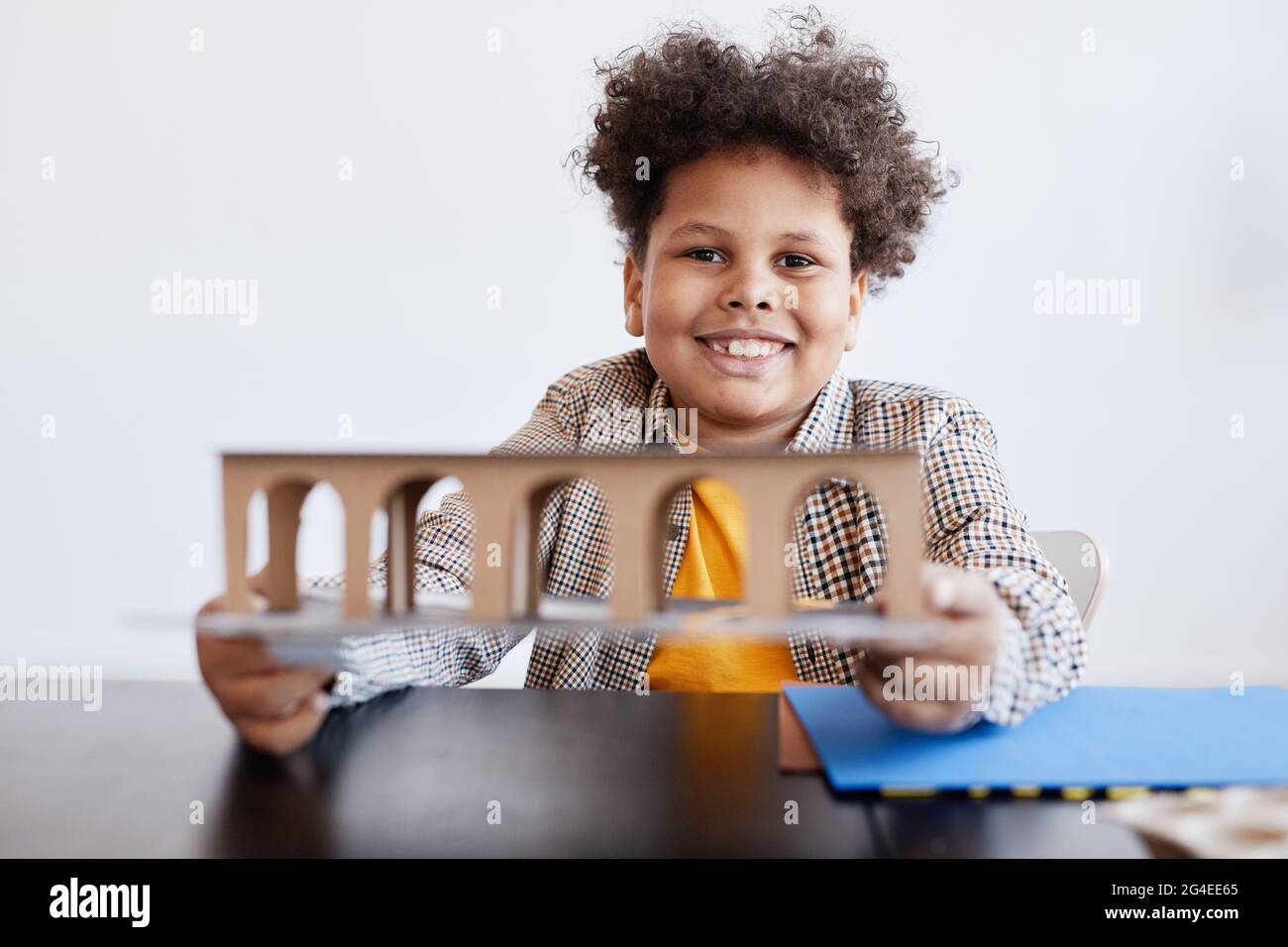 Vista frontale ritratto di sorridente afroamericano ragazzo tenendo in mano il modello di cartone mentre si lavora su un progetto di scuola artigianale, copia spazio Foto Stock