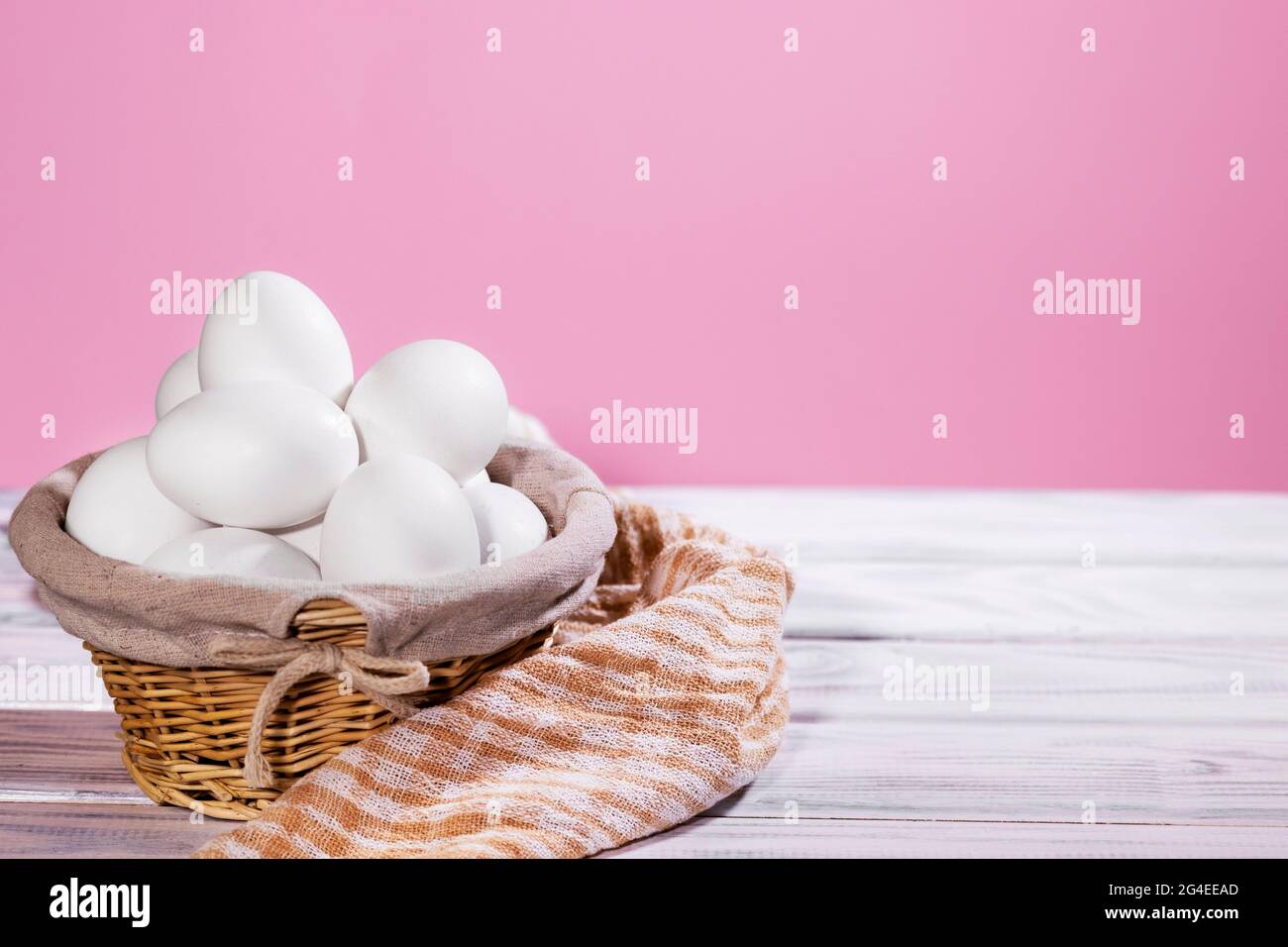 Pollo bianco eggsin un cestino di paglia su sfondo rosa con pezzo di stoffa, prodotto naturale Foto Stock