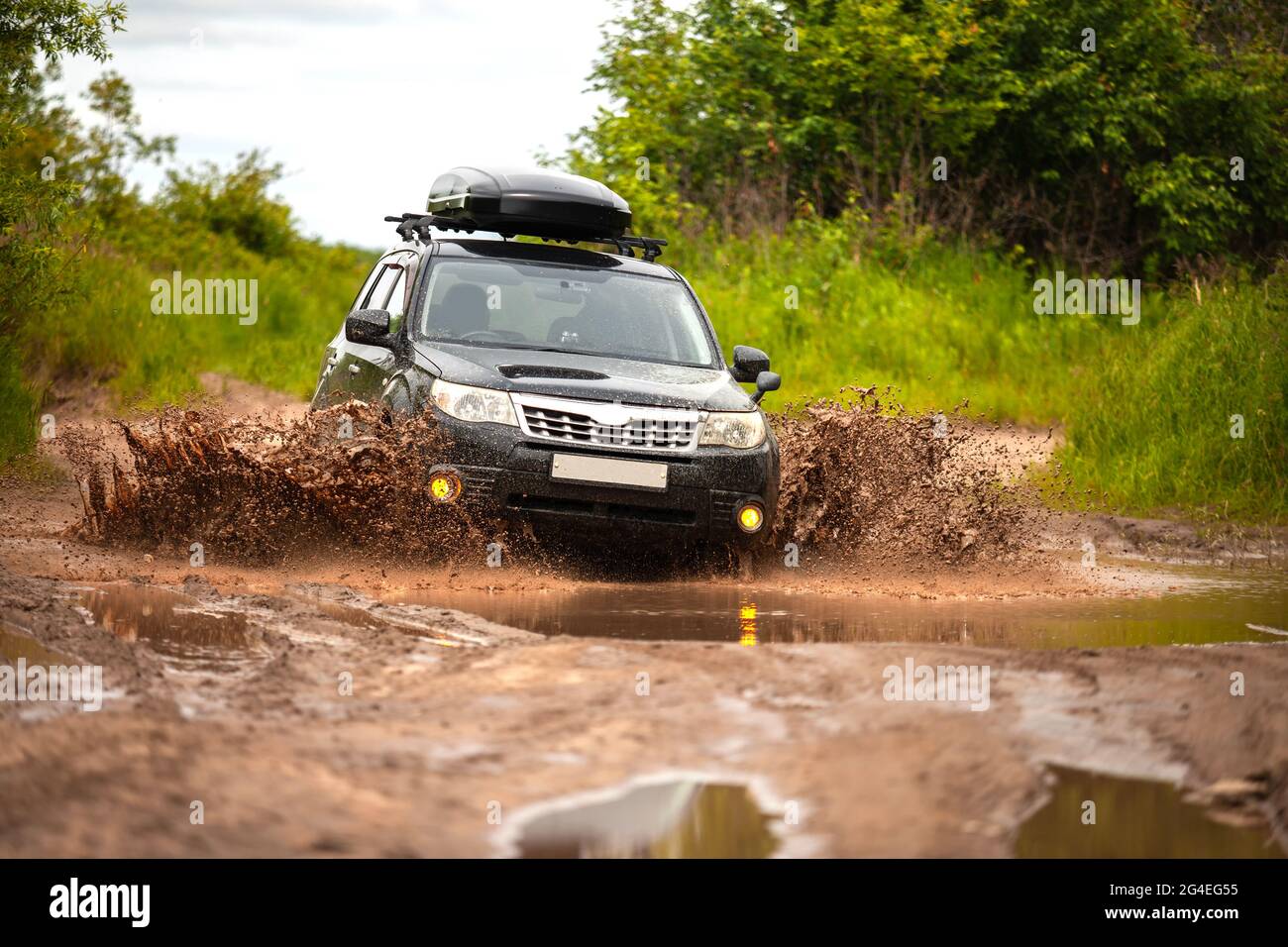 Black Subaru Forester che si muove su strada forestale sporca facendo un sacco di spruzzi d'acqua Foto Stock