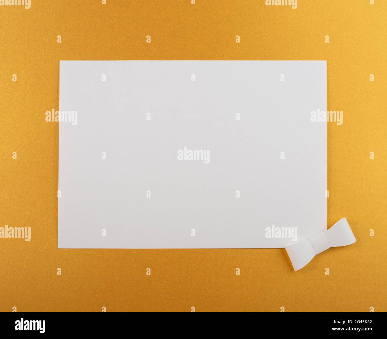 Foglio di carta su sfondo oro con nastro bianco. Composizione orizzontale di posa piatta con spazio di copia. Layout creativo, riprese in studio. Foto Stock