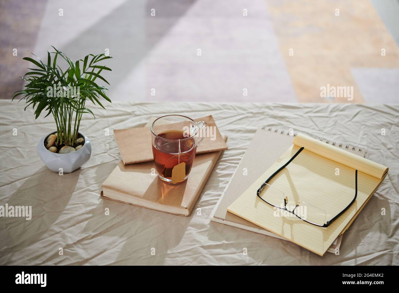 Tazza di tè, pianificatore, bicchieri e pianta in pentola su tavola coperta di tovaglia sbriciolato Foto Stock