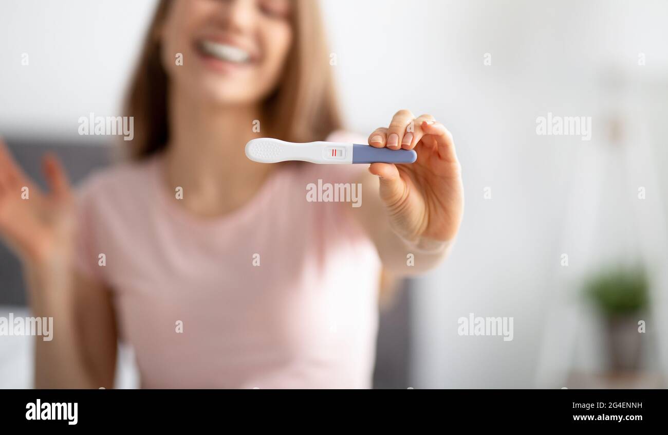 Primo piano di una giovane donna che mostra un test di gravidanza positivo  alla fotocamera, sensazione di essere felice di avere il bambino a casa,  fuoco selettivo Foto stock - Alamy