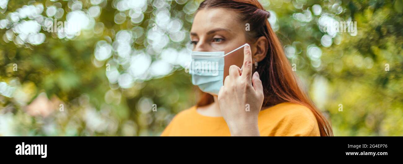 Rilassata ragazza felice toglie la sua maschera medica protettiva dal viso per respirare aria fresca dopo la fine della pandemia coronavirus. Niente di più Foto Stock