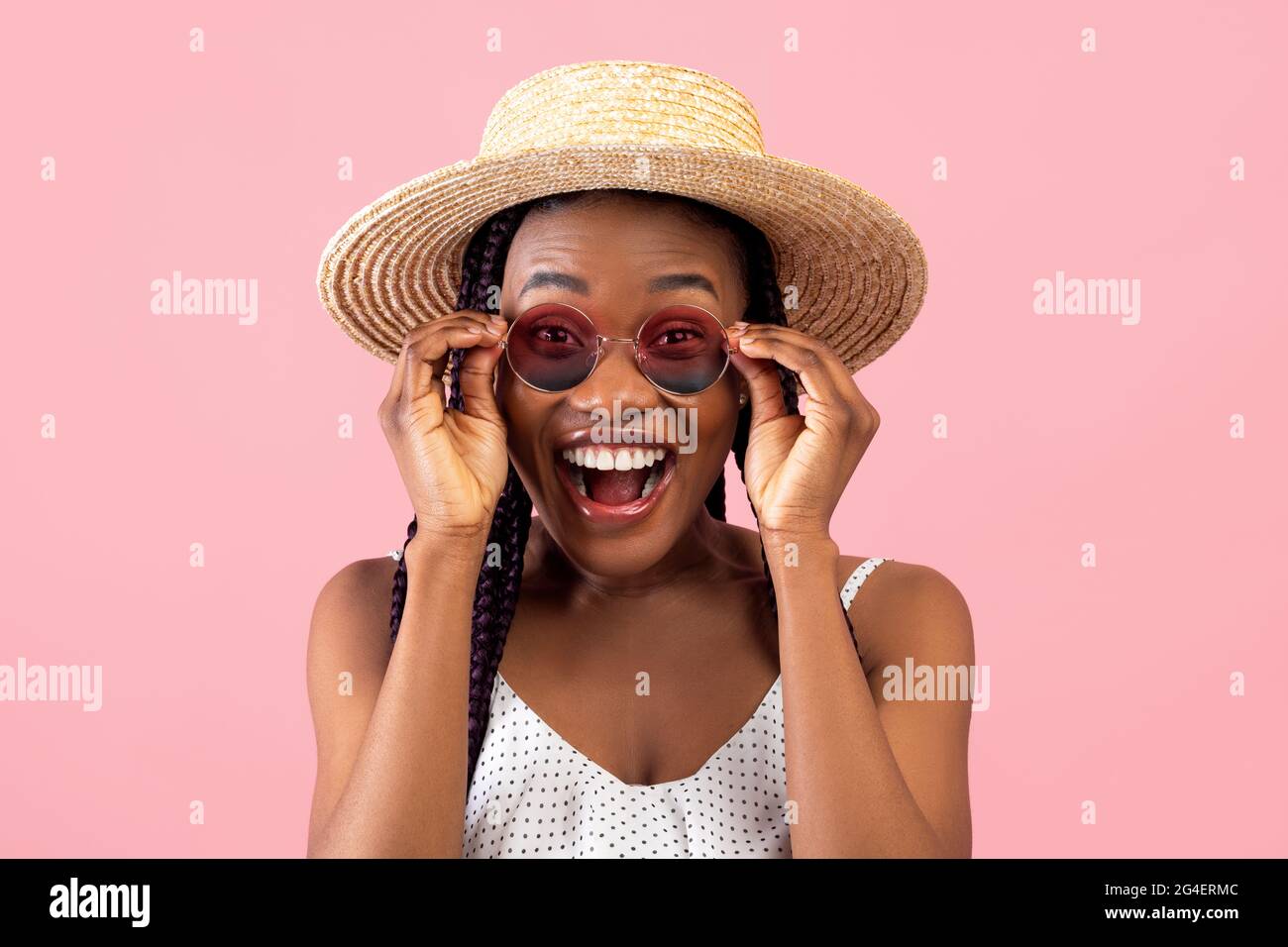 Eccitata donna afroamericana millenaria in estate indossa i suoi occhiali da sole, gridando WOW su sfondo rosa Foto Stock