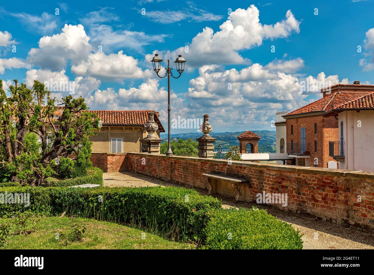 Cespugli verdi nel parco e case tipiche sotto il bel cielo blu con nuvole bianche nella piccola città di Govone in Piemonte, Italia settentrionale. Foto Stock