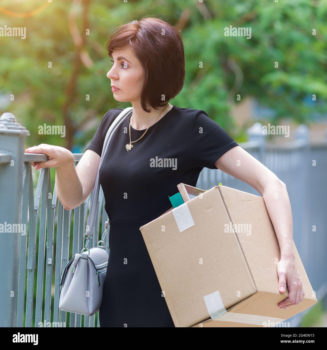 Una donna infornata con scatola degli effetti personali sta al pensiero della recinzione. Foto Stock