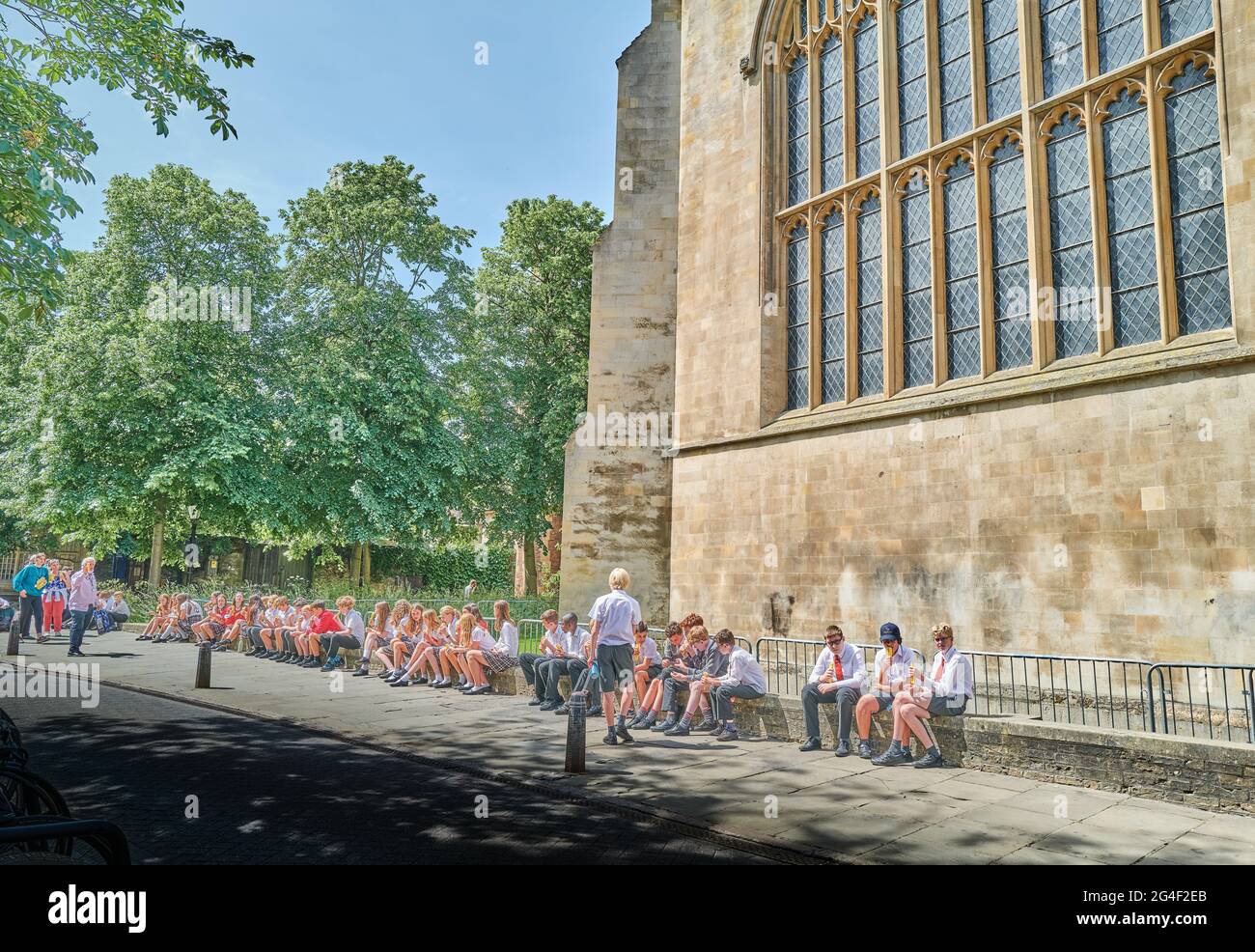 Gruppo di bambini si siedono e si rilassano sulla parete bassa fuori della cappella del Trinity College, l'università di Cambridge, Inghilterra, in una giornata estiva soleggiata. Foto Stock