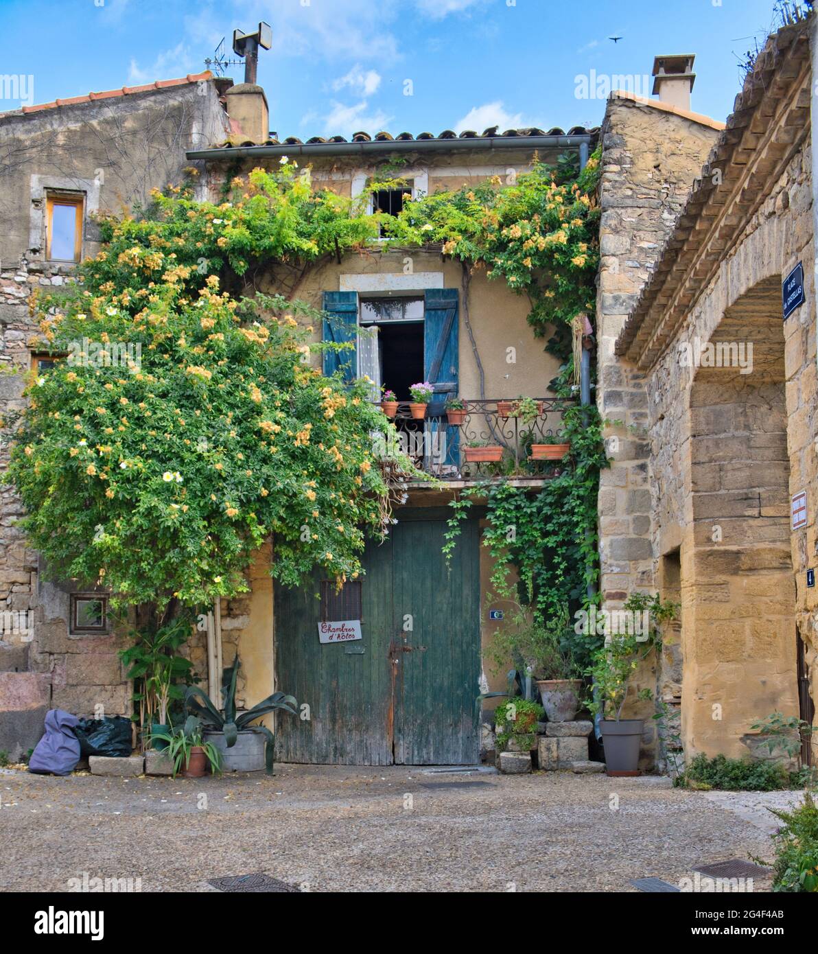 Collias, Provence, France 06.21.21 edificio rustico in pietra con porte doppie in legno verde. Finestra e balcone con persiane blu. Piante pareti di arrampicata Foto Stock