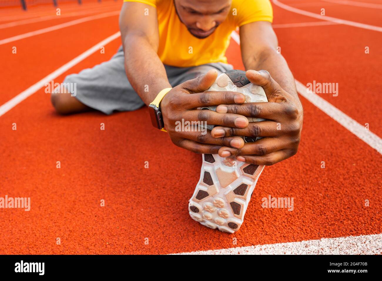 Primo piano african american giovane maschio seduto allo stadio che allunga le gambe su sfondo luminoso. Giovane uomo nero professionale in gialle sportive Foto Stock