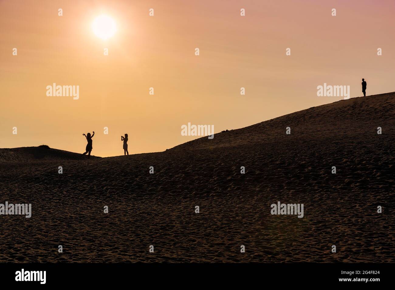 Tre persone su una duna, donna che scattano foto di donna, uomo che guarda, silhouette al tramonto, Nordjylland, Jutland del Nord, Danimarca Foto Stock