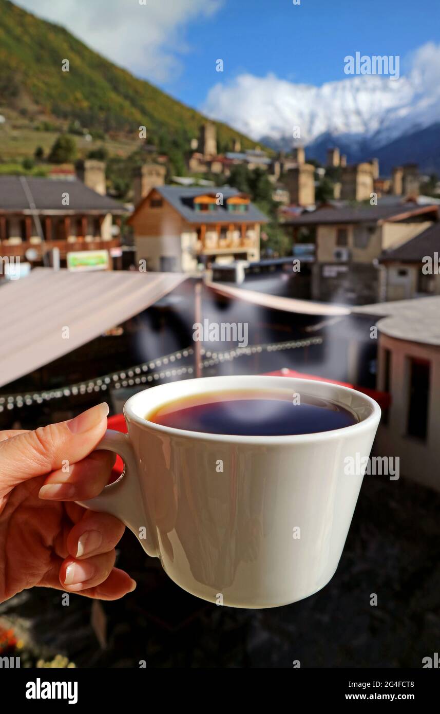 Mano femminile che tiene una tazza di caffè caldo con vapore contro la vista di paese sfocata Foto Stock