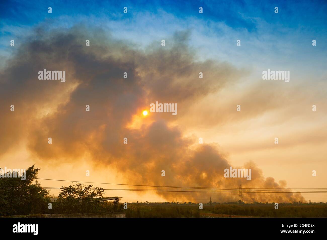 Il fumo che esce dalle fabbriche all'orizzonte, l'inquinamento dell'aria si sta diffondendo come nuvole e coprendo il sole che tramonta. Sparato al villaggio rurale di WB, India. Foto Stock