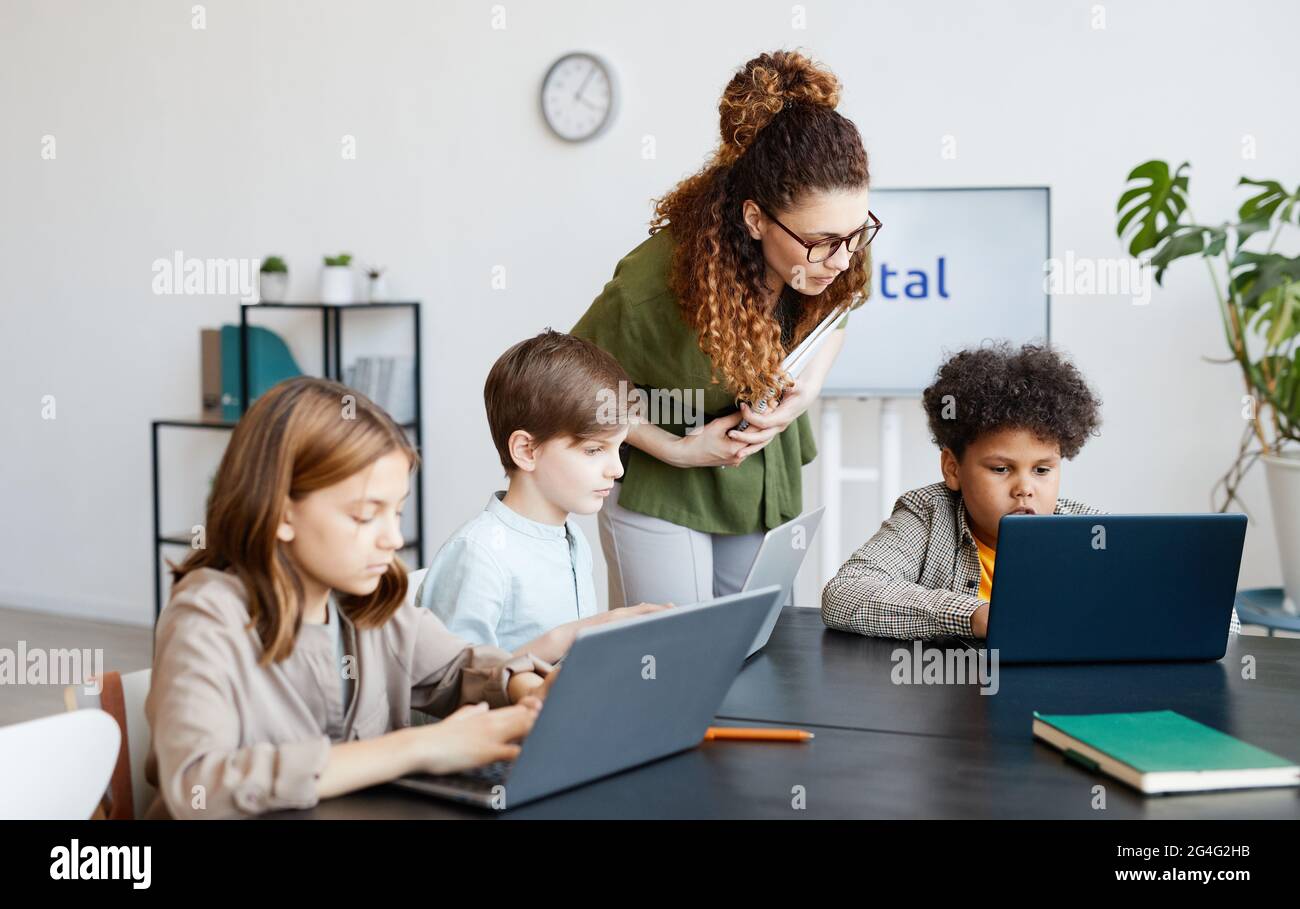 Gruppo diversificato di bambini che usano il computer durante LA lezione DI  INFORMATICA a scuola con una giovane insegnante femminile Foto stock - Alamy
