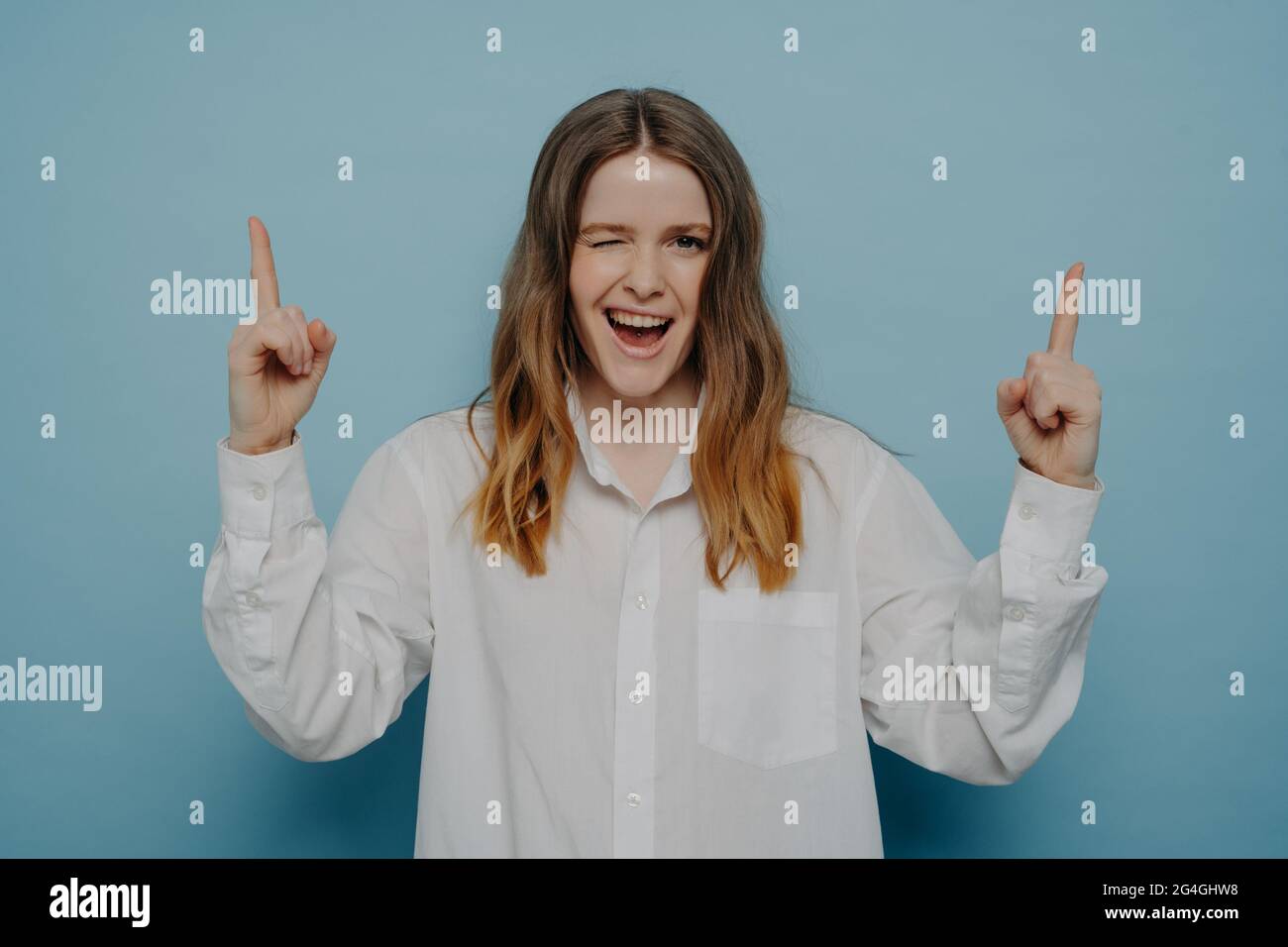 Winking felice ragazza adolescente che si pone contro parete blu Foto Stock