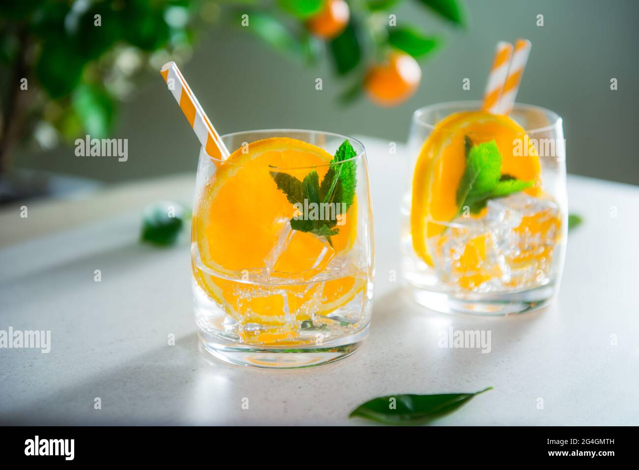 Due rinfrescanti cocktail di frutta con arancia, menta e ghiaccio su tavola bianca con sfondo di agrumi. Bevande estive da bar. Fuoco selettivo, copia Foto Stock