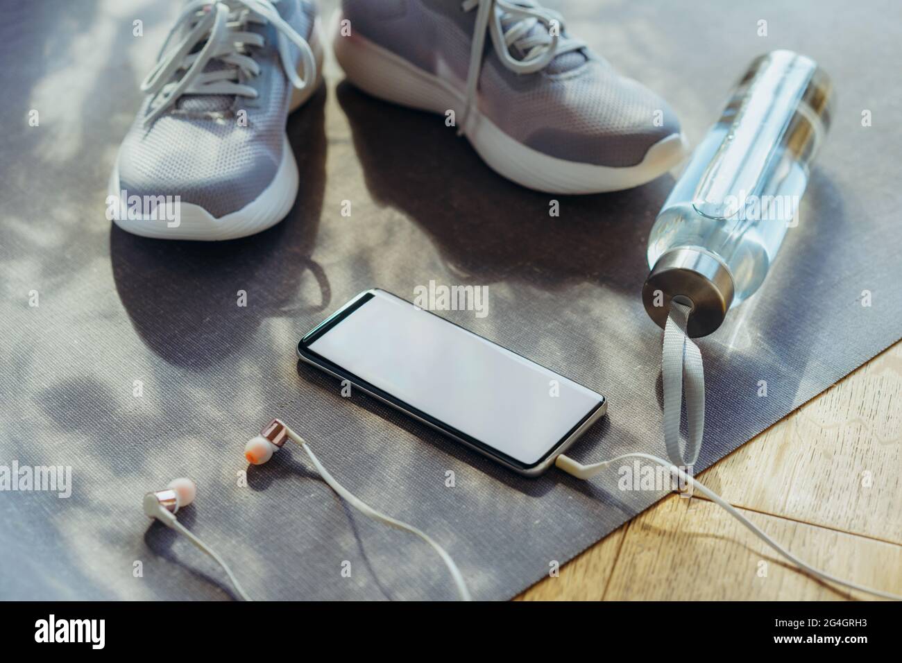 Schermo vuoto per smartphone con auricolari, bottiglia con acqua e sneaker sullo sfondo. Set per running e attività sportive . Sano e attivo Foto Stock