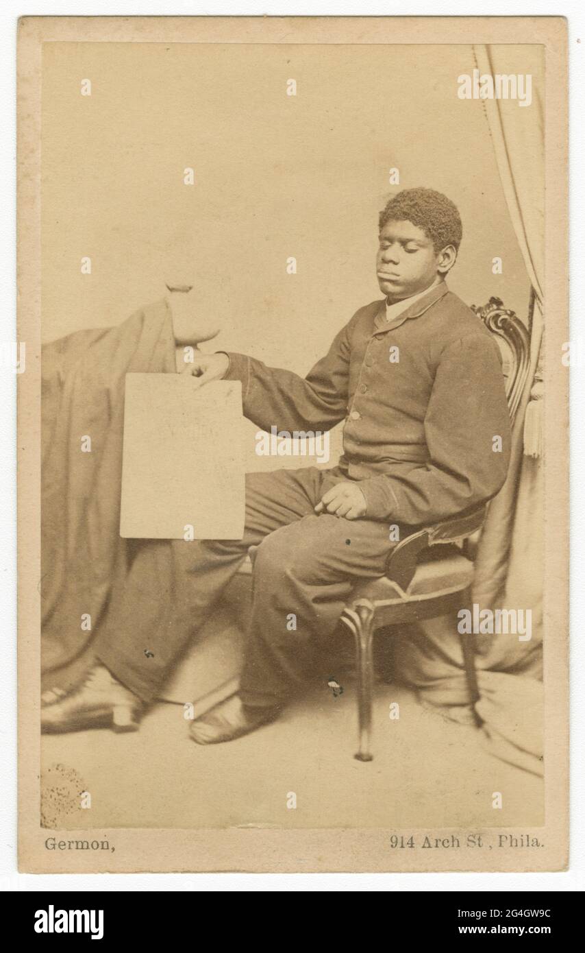 Una stampa di albume bruno giallognolo cartes-de-visite fotografia della prodigio musicale afro-americano Thomas Wiggins (1849-1908), uno dei pianisti americani più conosciuti del 19 ° secolo. Ha pubblicato numerose composizioni originali e ha avuto una lunga e riuscita carriera di performante in tutti gli Stati Uniti. È seduto su una sedia con il lato sinistro rivolto verso la telecamera. Sta tenendo un pezzo di carta con la mano destra. La mano sinistra poggia sul ginocchio. Un tessuto si trova sul lato sinistro della fotografia. Una tenda si trova sul lato destro della fotografia. Un tessuto è sulla sinistra Foto Stock