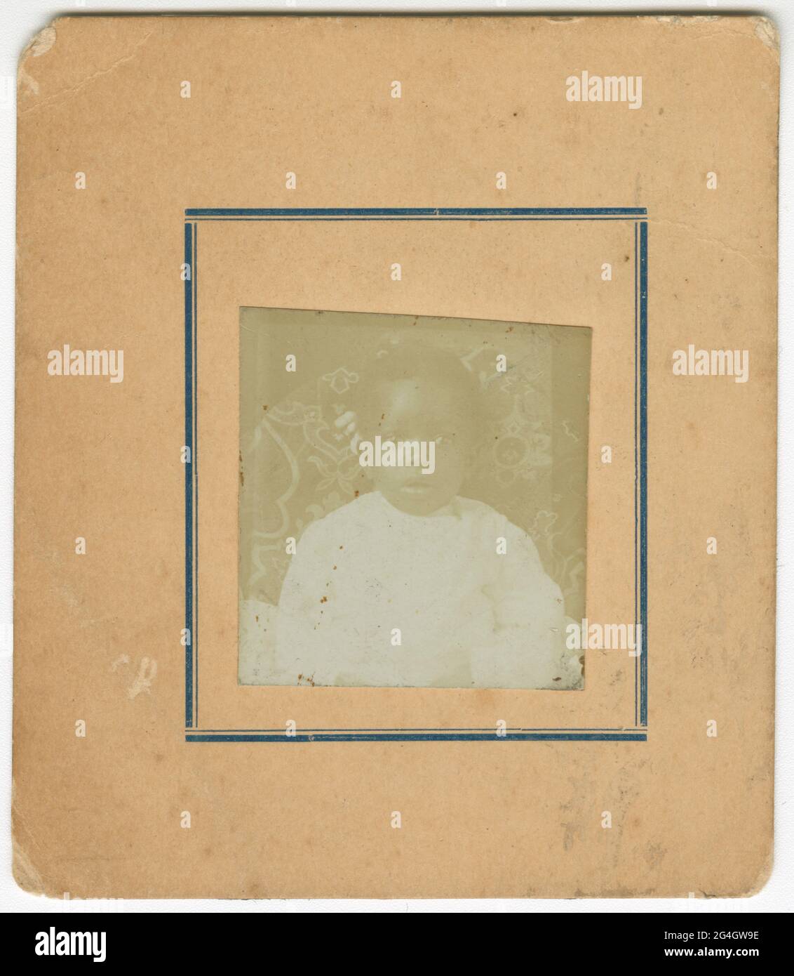 Una foto di un bambino afroamericano vestito di abiti bianchi con i toni del seppia cartes-de-visite. Il bambino è seduto su una sedia con motivi floreali e guarda la macchina fotografica. La fotografia è in una carta color crema con due linee che si affacciano sull'immagine. La linea interna è sottile mentre la linea esterna è molto più spessa. Non sono presenti iscrizioni sulla parte anteriore o posteriore. Foto Stock